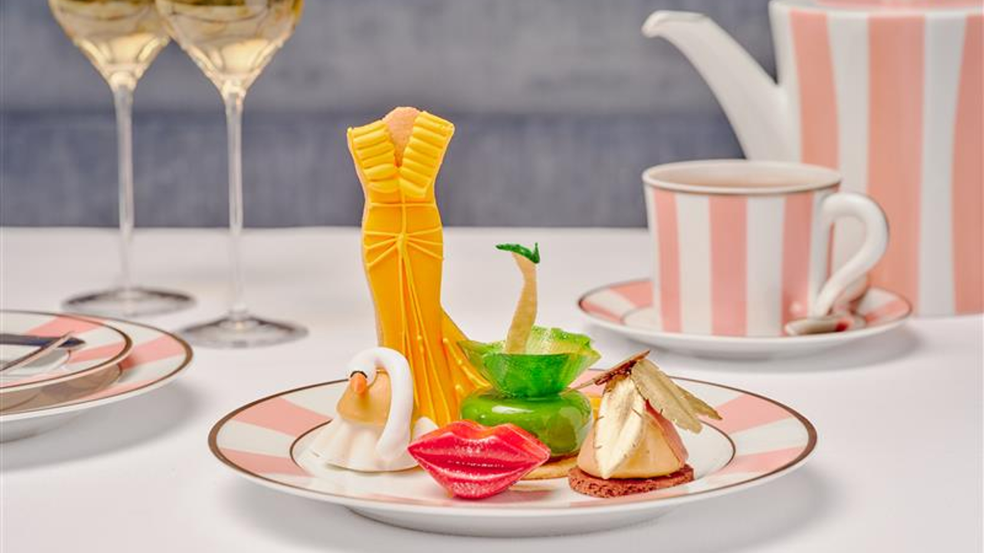 A plate of fashion-themed pastries served with tea and champagne in pink-striped china.