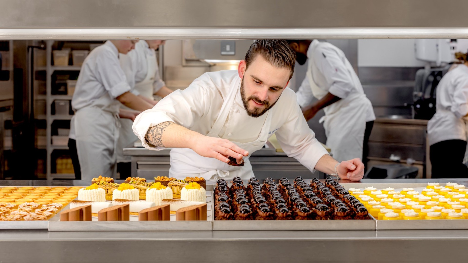 A pastry chef carefully places finishing touches on exquisite desserts in a bustling, professional kitchen.