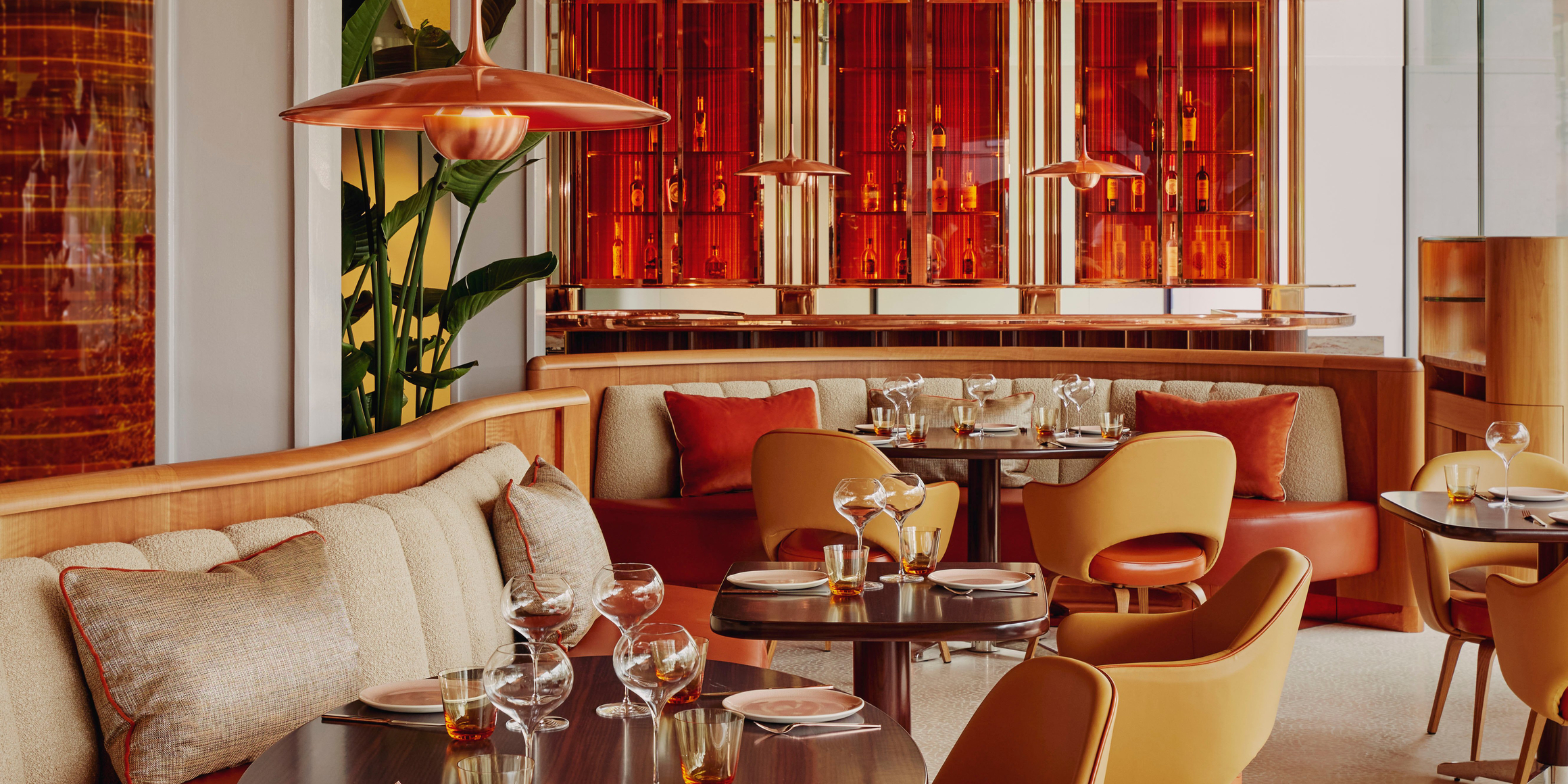 Contemporary dining space with warm tones, curved seating, stylish pendant lights, and vibrant red accents creating a modern ambiance.