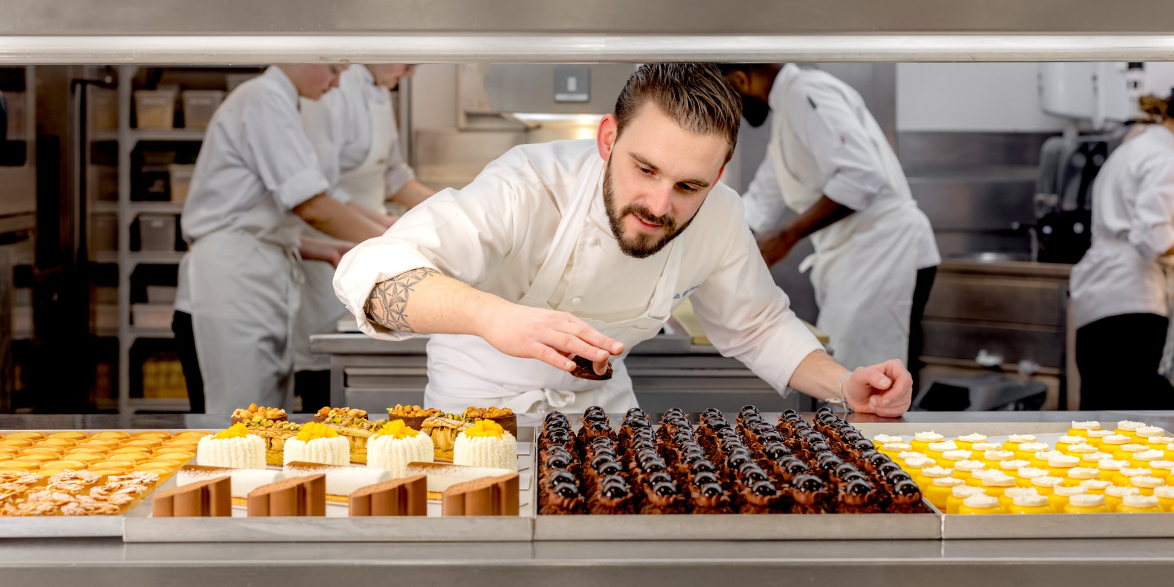 A pastry chef carefully places finishing touches on exquisite desserts in a bustling, professional kitchen.