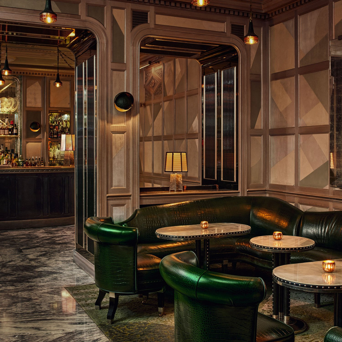 Elegant lounge with rich green leather seating, marble tables, and warm lighting, creating an inviting, sophisticated ambiance.
