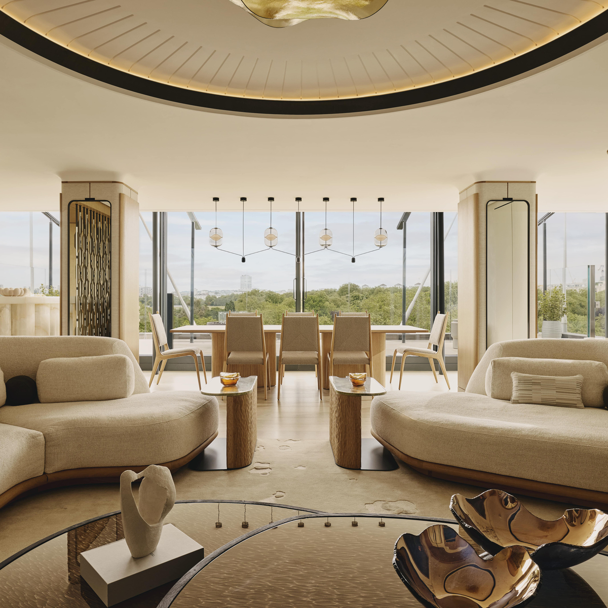 A modern, light-filled penthouse with curved sofas, a dining area, and floor-to-ceiling windows overlooking lush greenery.