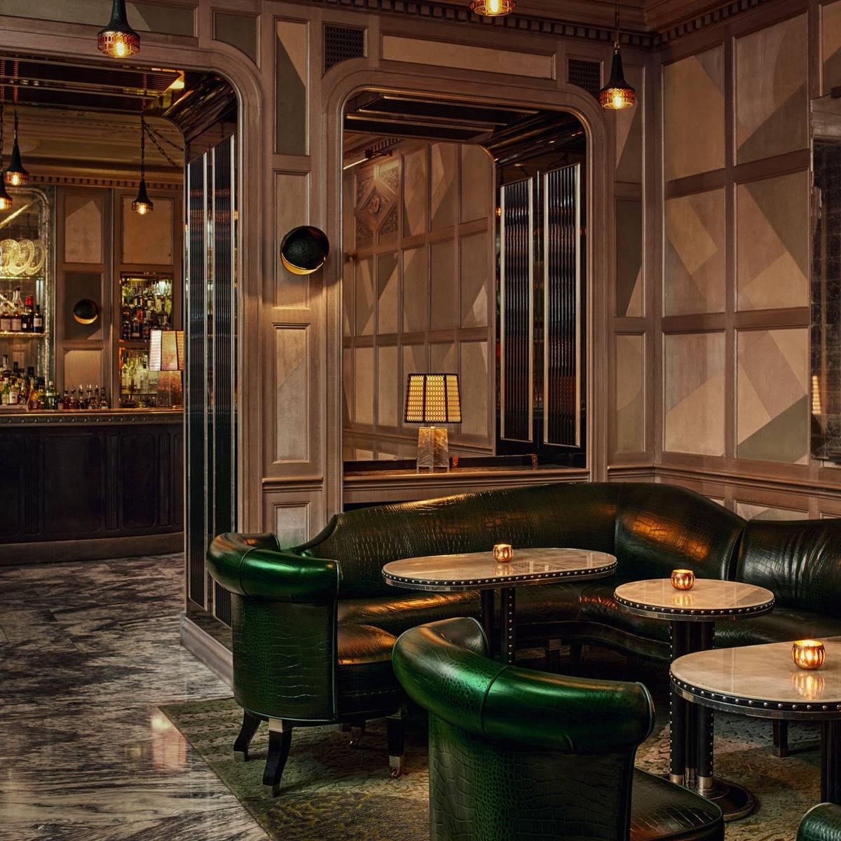 Elegant lounge with rich green leather seating, marble tables, and warm lighting, creating an inviting, sophisticated ambiance.