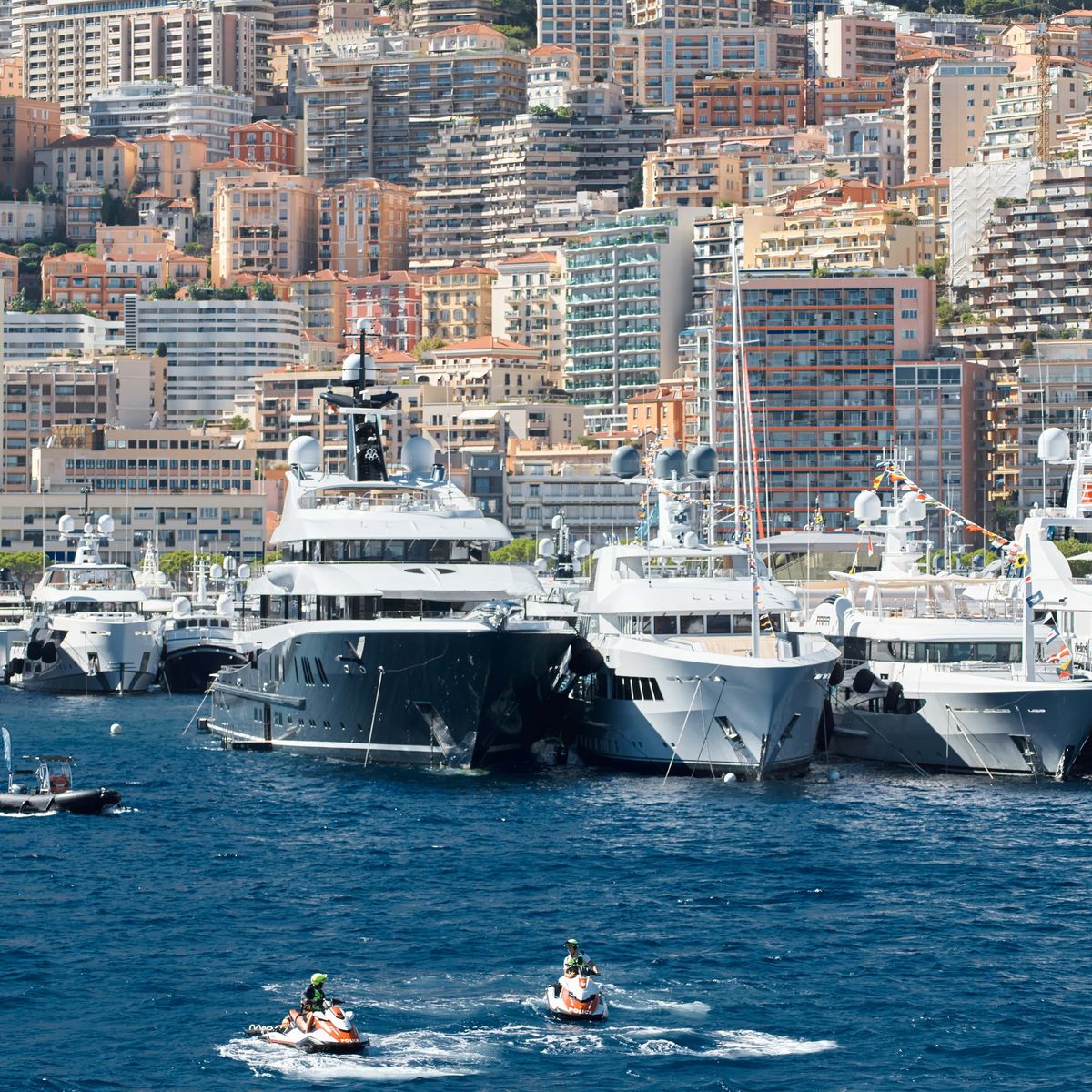 A dazzling display of superyachts moored against Monaco’s hillside skyline, with jet skis gliding across the deep blue water.