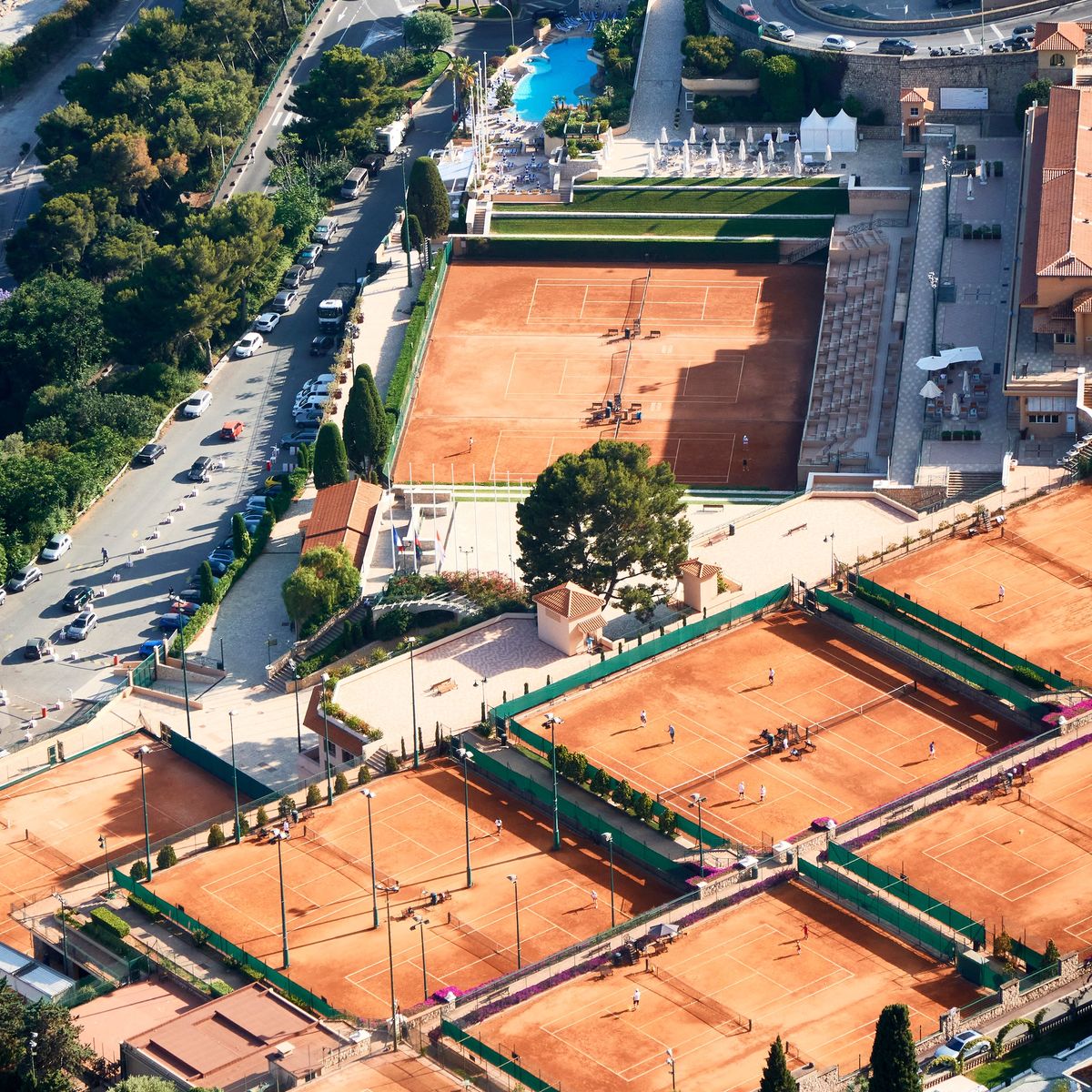 Aerial view of Monte Carlo's red clay tennis courts nestled between lush greenery and the shimmering coastline