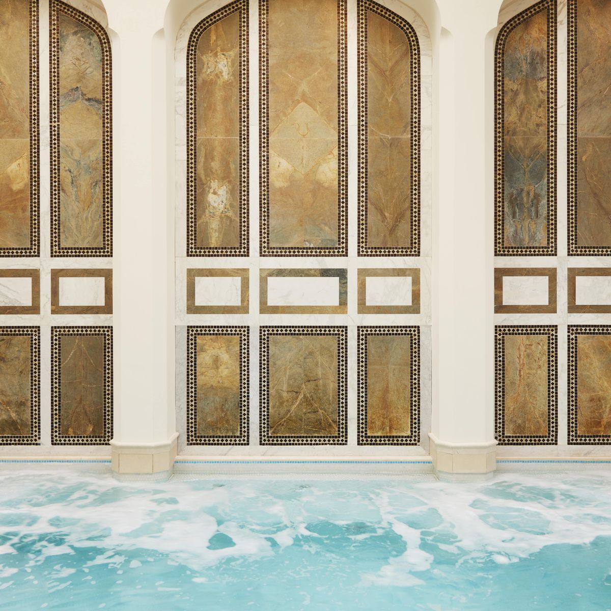 Elegant indoor spa pool with ornate arched wall panels, soothing turquoise water, and skylights creating a serene atmosphere