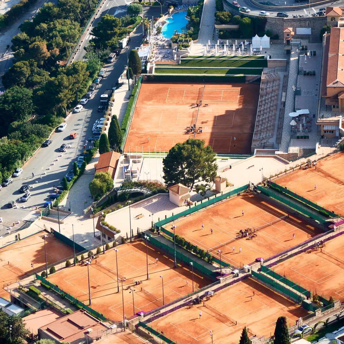 Aerial view of Monte Carlo's red clay tennis courts nestled between lush greenery and the shimmering coastline