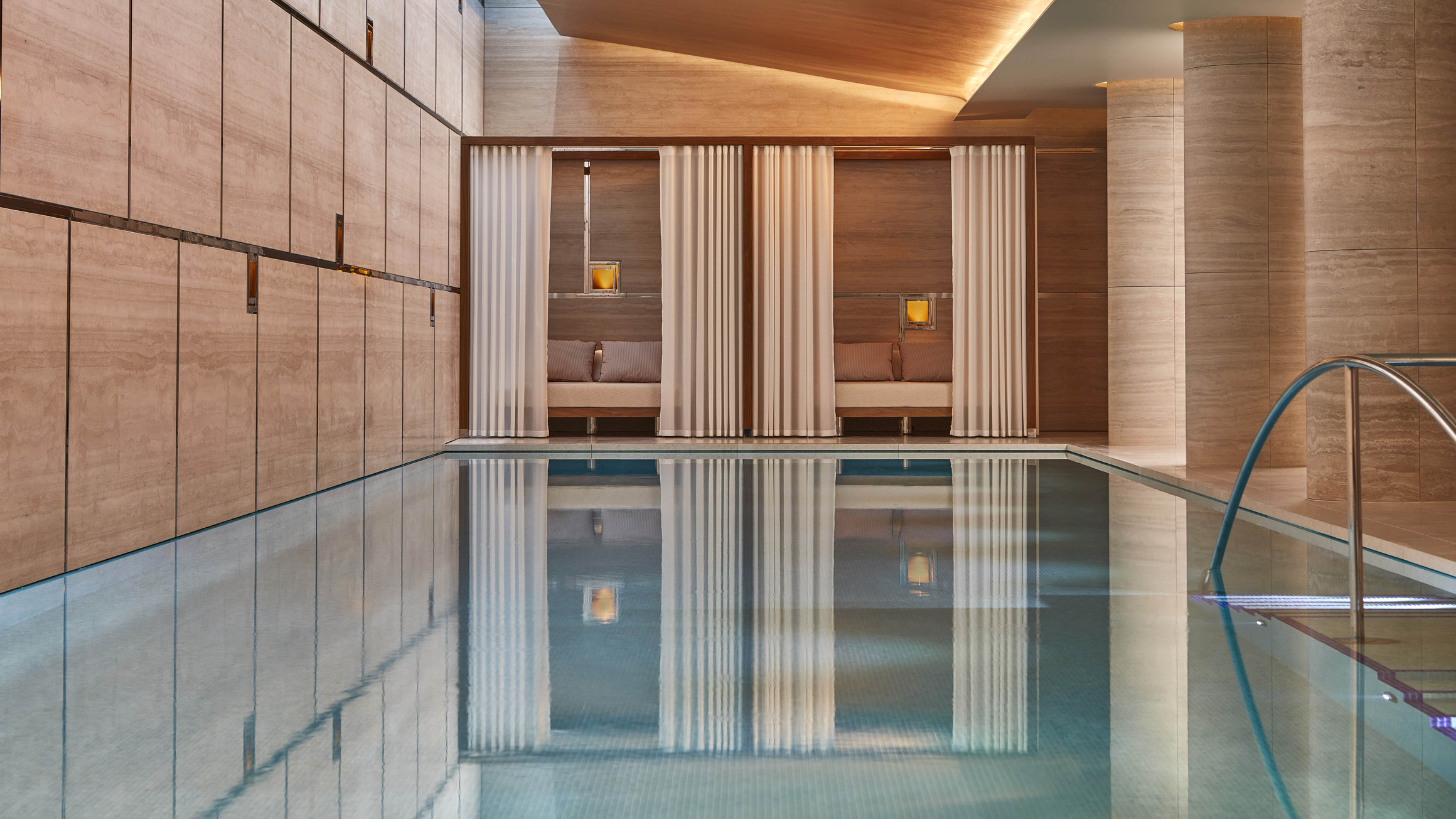 Luxurious indoor pool with serene cabanas, soft curtains, and warm wood tones, creating a tranquil and refined retreat.