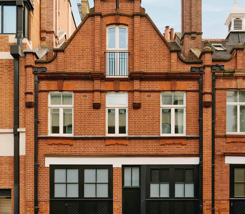 A red-brick townhouse with black garage doors, white-framed windows, and decorative topiary in a serene courtyard.
