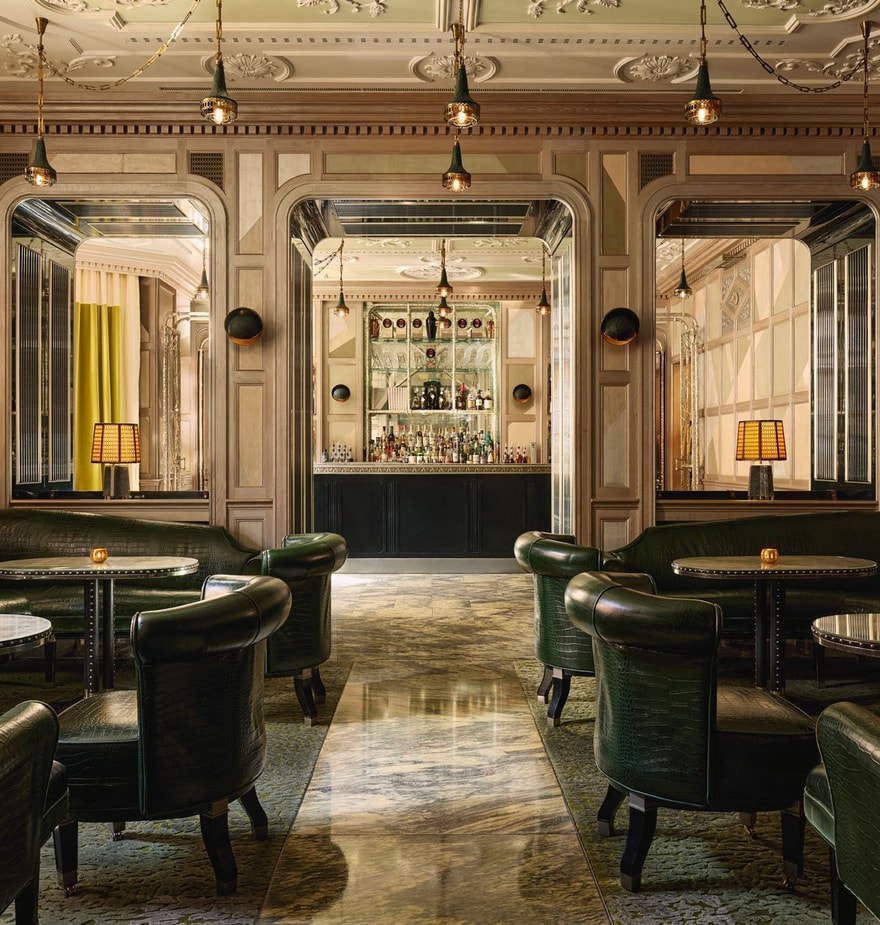An elegant bar with dark green leather seating, marble floors, mirrored panels, and soft lighting, creating a refined, intimate ambiance.
