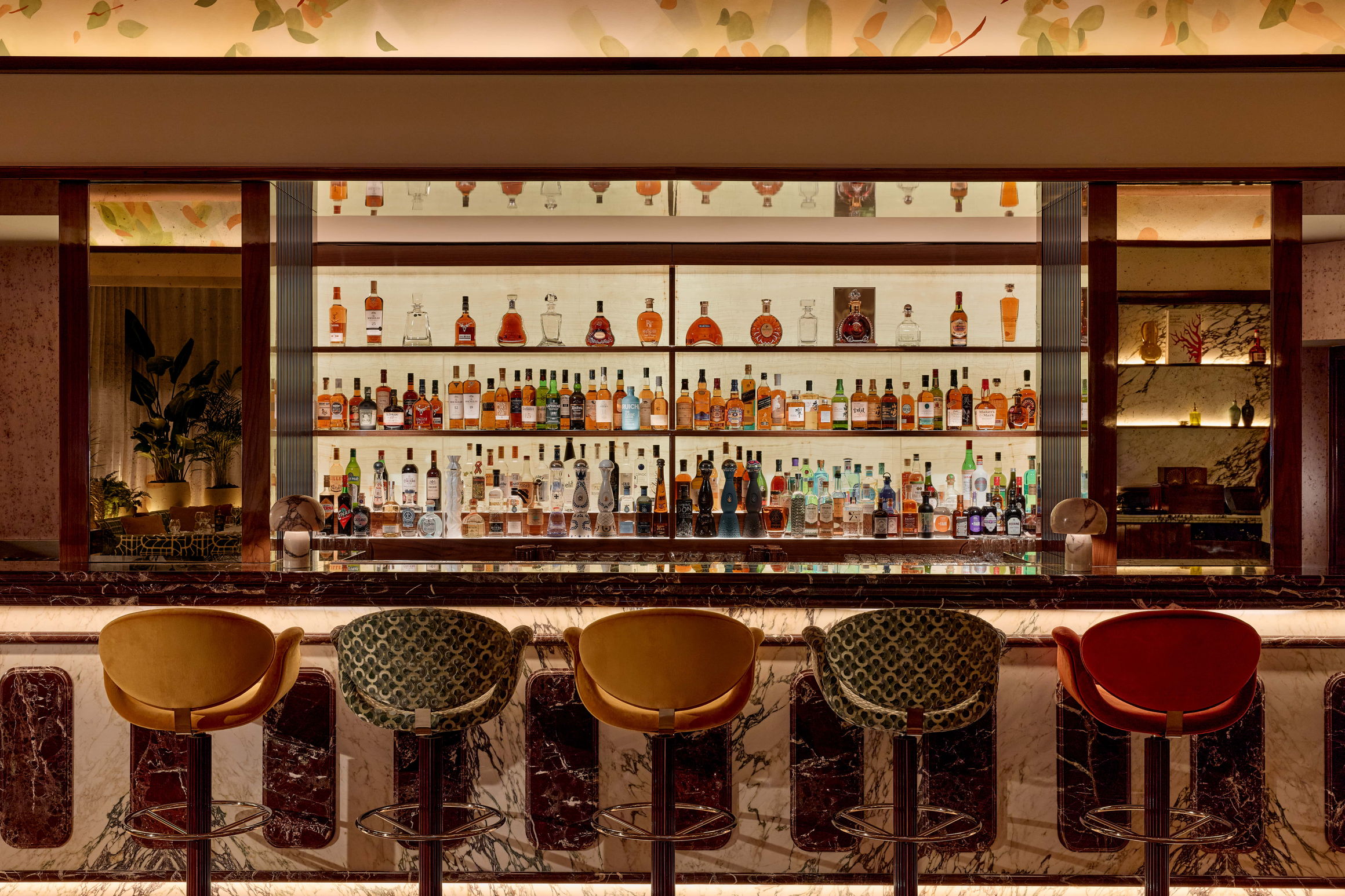 Sophisticated bar with a marble counter and a colourful selection of spirits on backlit shelves.