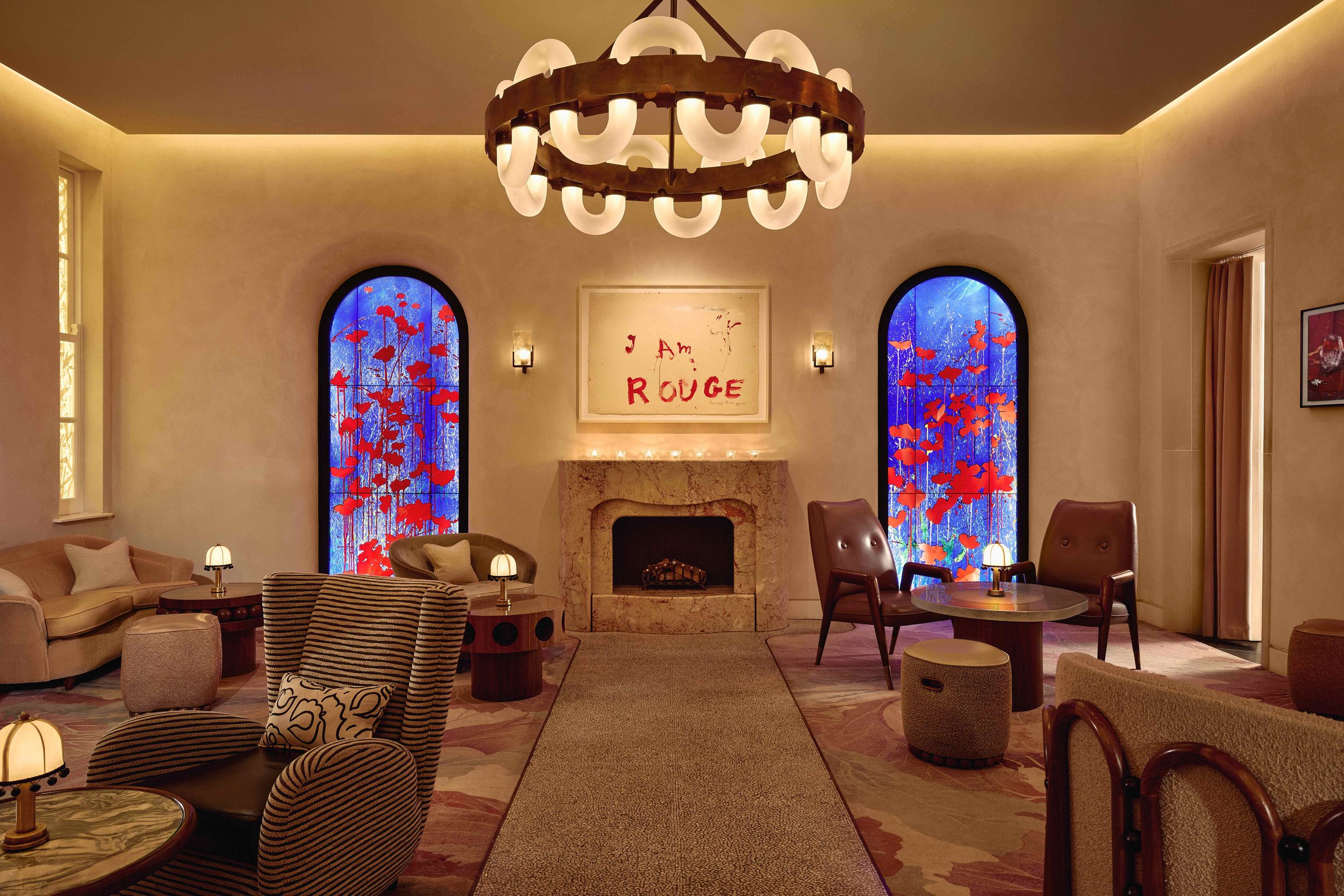 Elegant lounge with modern furniture, marble fireplace, bold artwork, and two vibrant stained-glass windows featuring red flowers on blue.