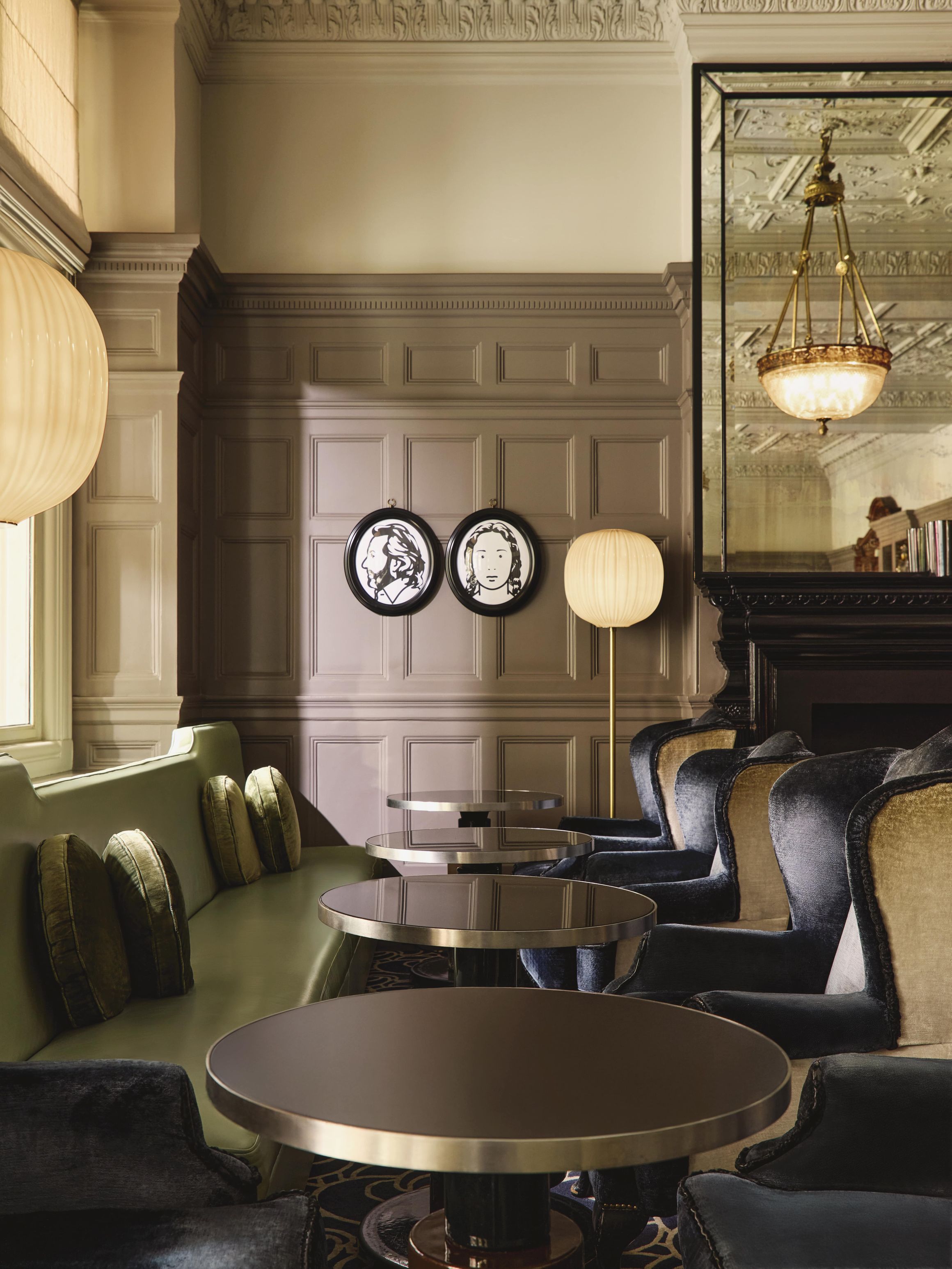 Chic lounge with velvet seating, round tables, and decorative wall portraits in a heritage-style interior.