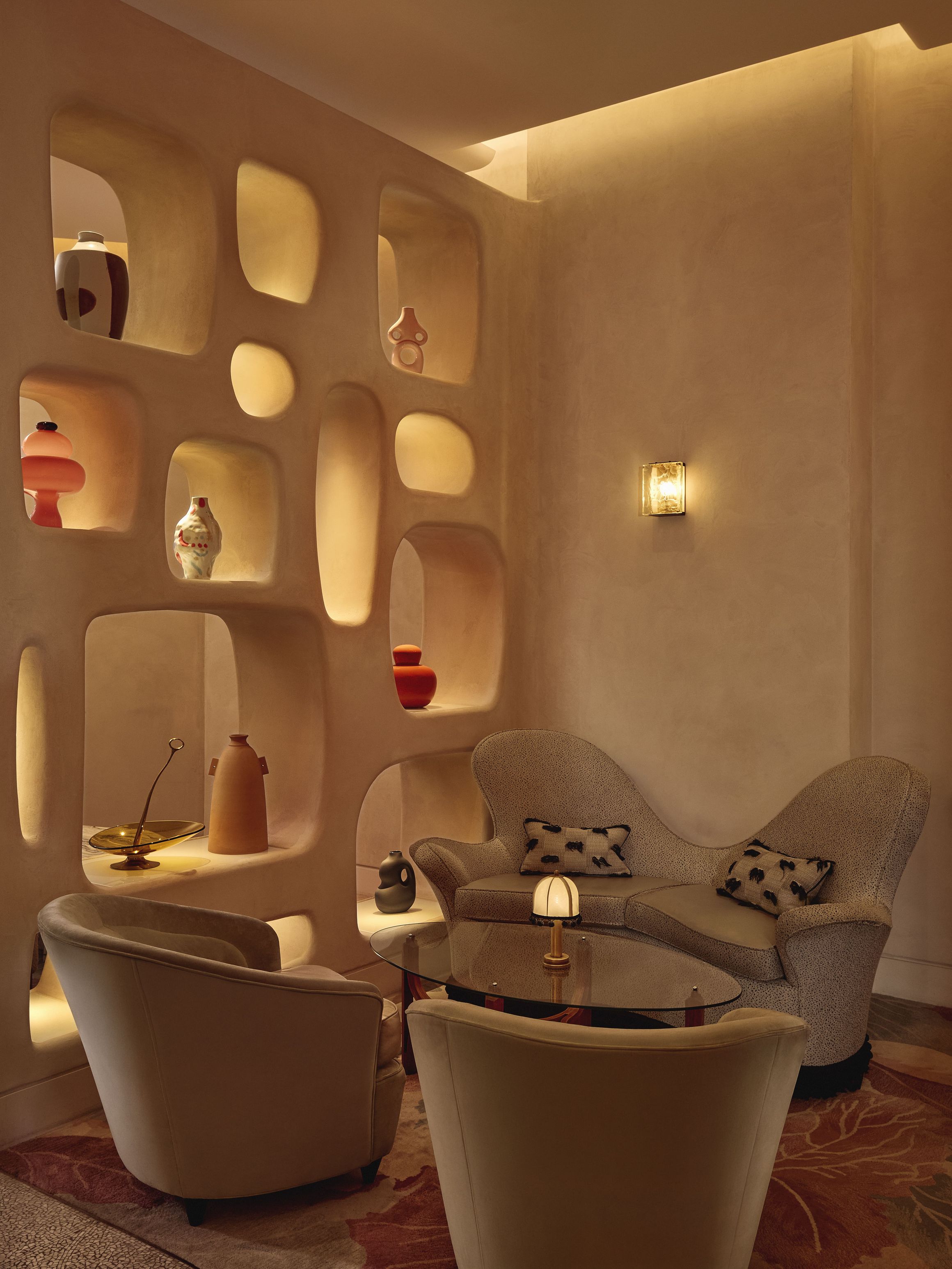 Curved lounge seating with sculptural shelving and warm lighting in a contemporary, artful interior.