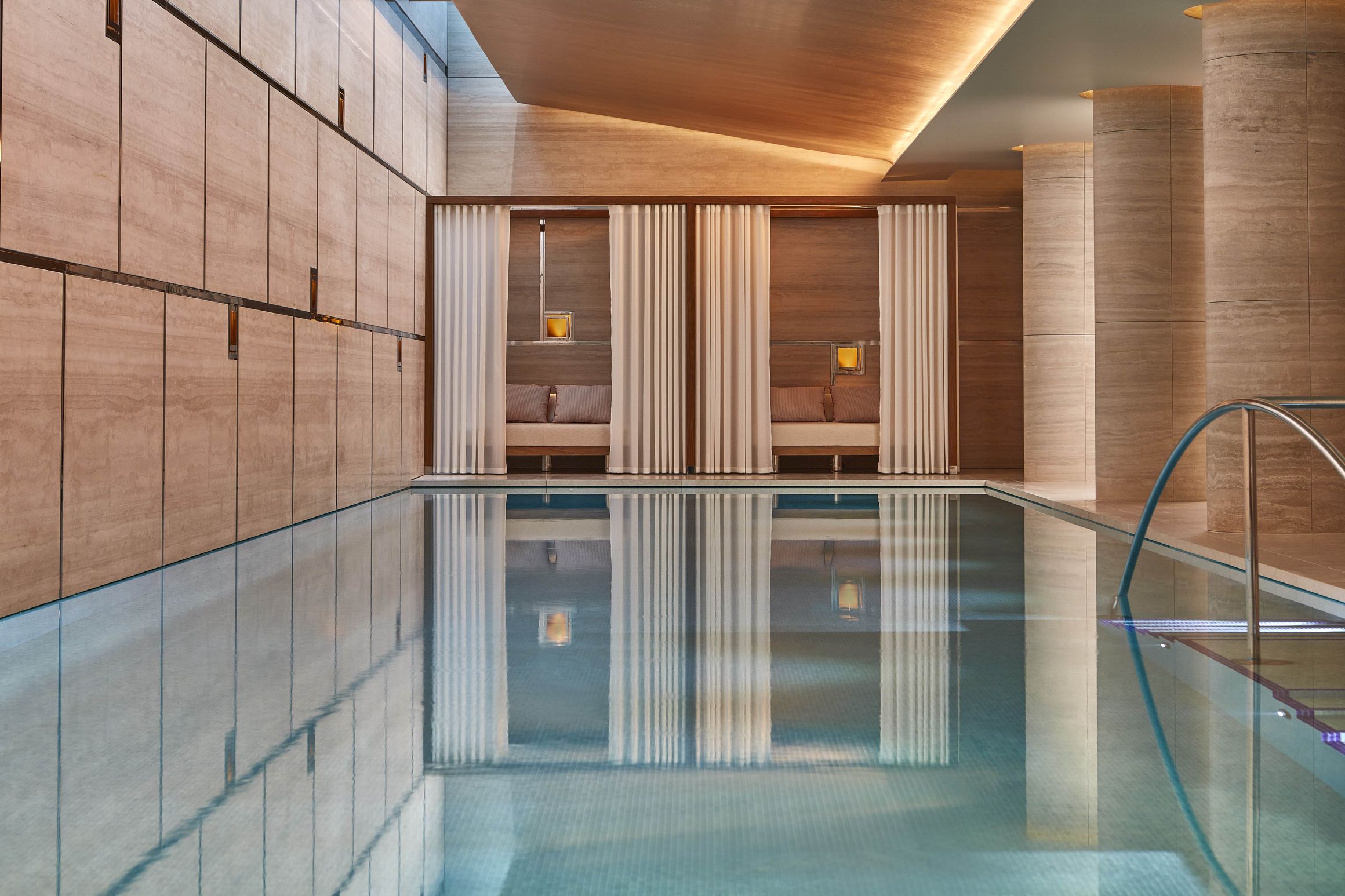 Luxurious indoor pool with serene cabanas, soft curtains, and warm wood tones, creating a tranquil and refined retreat.