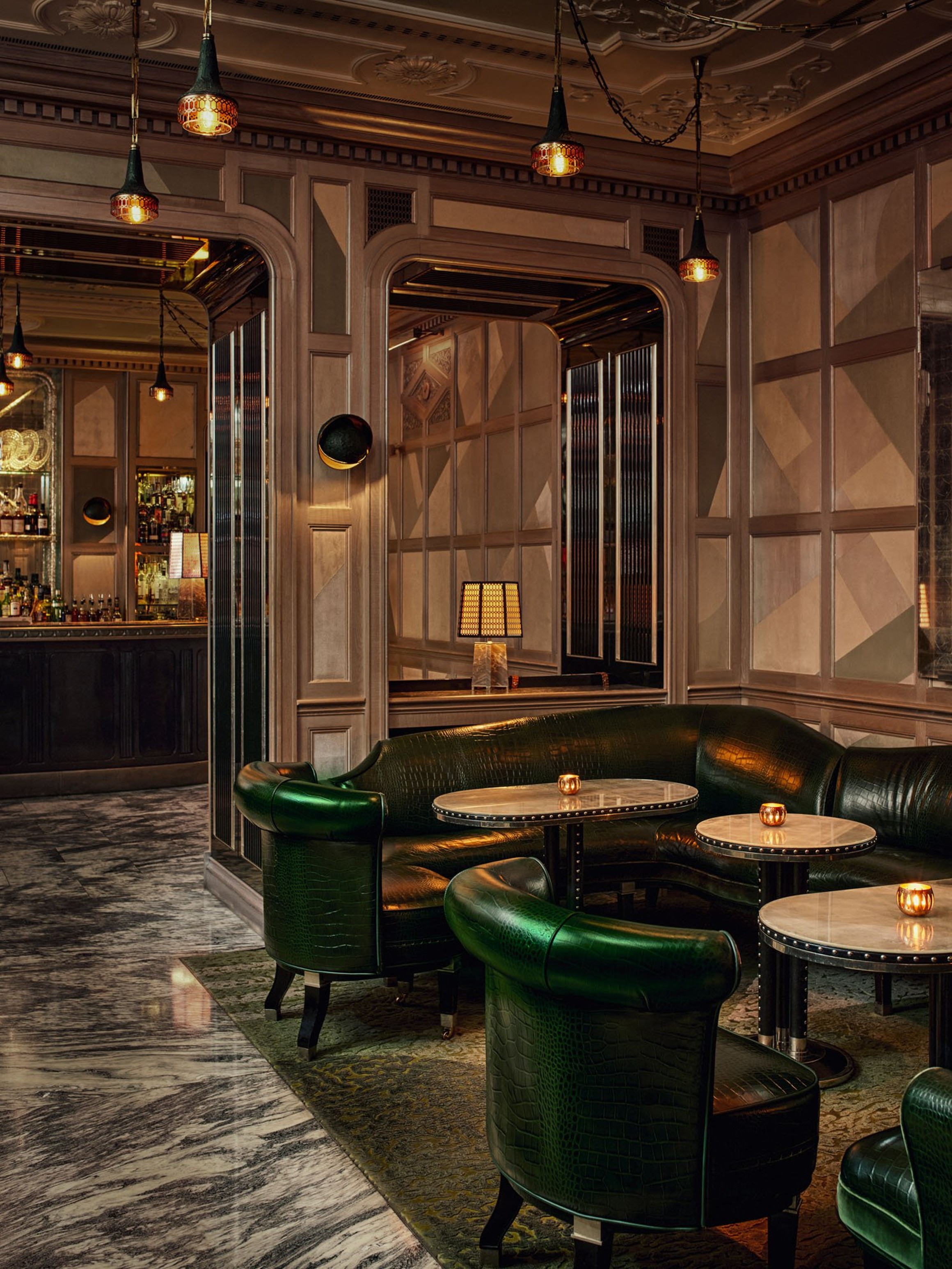 Elegant lounge with rich green leather seating, marble tables, and warm lighting, creating an inviting, sophisticated ambiance.