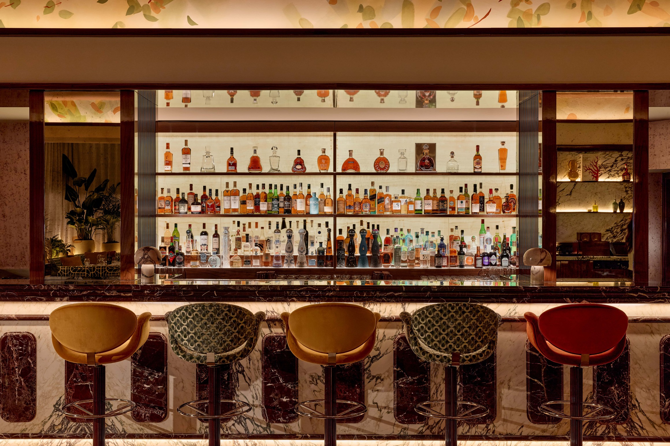 Sophisticated bar with a marble counter and a colourful selection of spirits on backlit shelves.