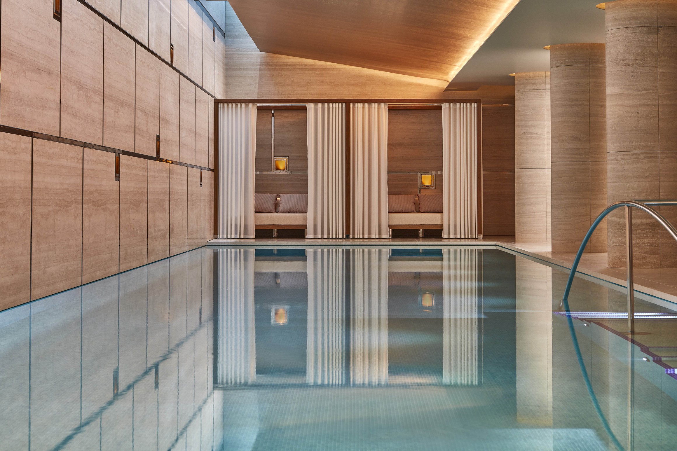 Luxurious indoor pool with serene cabanas, soft curtains, and warm wood tones, creating a tranquil and refined retreat.