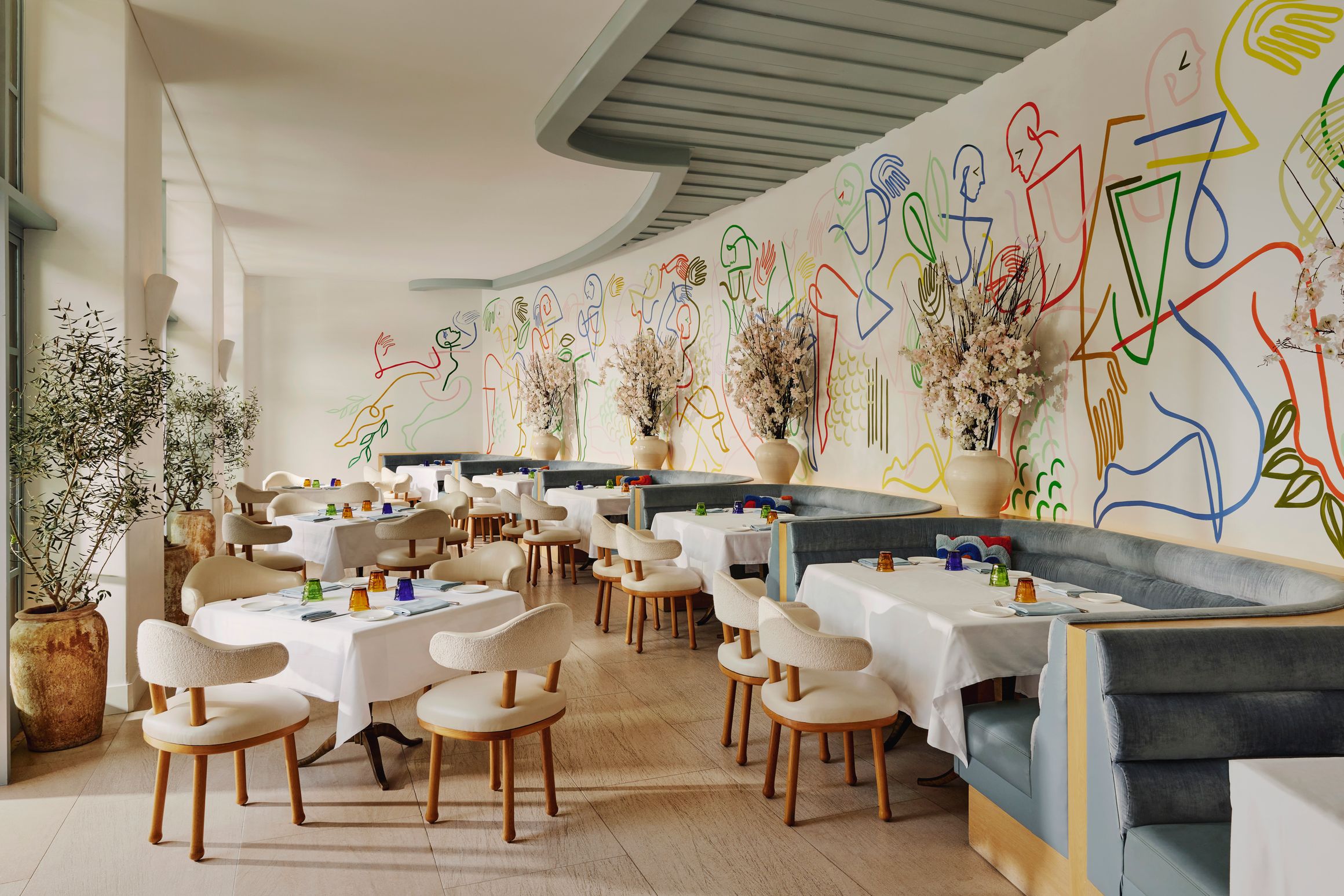 A stylish restaurant with contemporary decor, featuring a vibrant mural, plush seating, and elegantly set tables bathed in natural light.