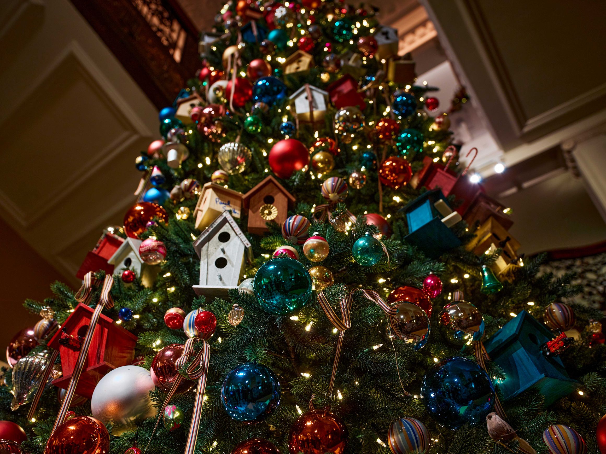 Close-up of Claridge’s 2024 Christmas tree with vibrant baubles, striped ribbons and handcrafted birdhouse ornaments.