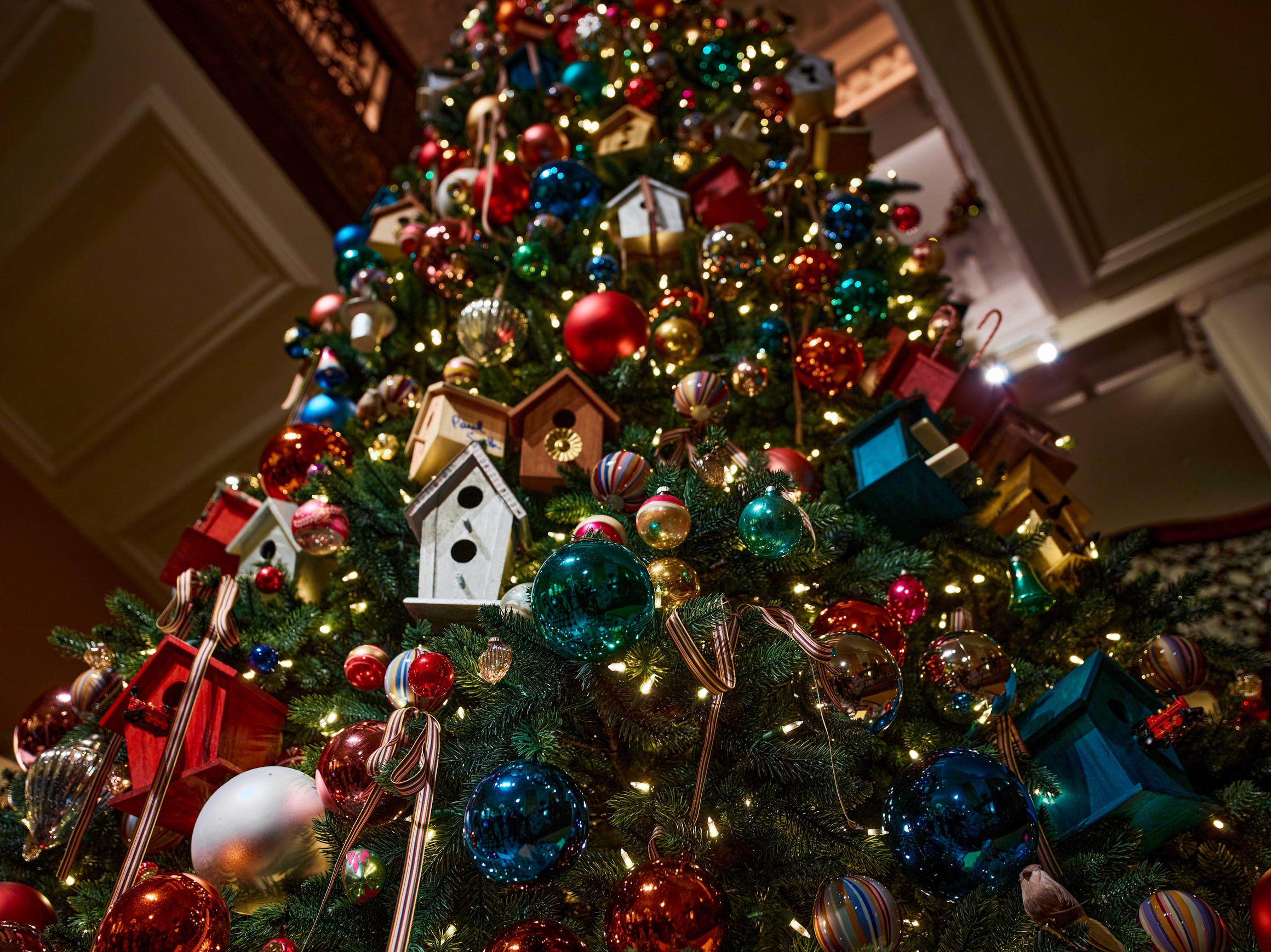 Close-up of Claridge’s 2024 Christmas tree with vibrant baubles, striped ribbons and handcrafted birdhouse ornaments.