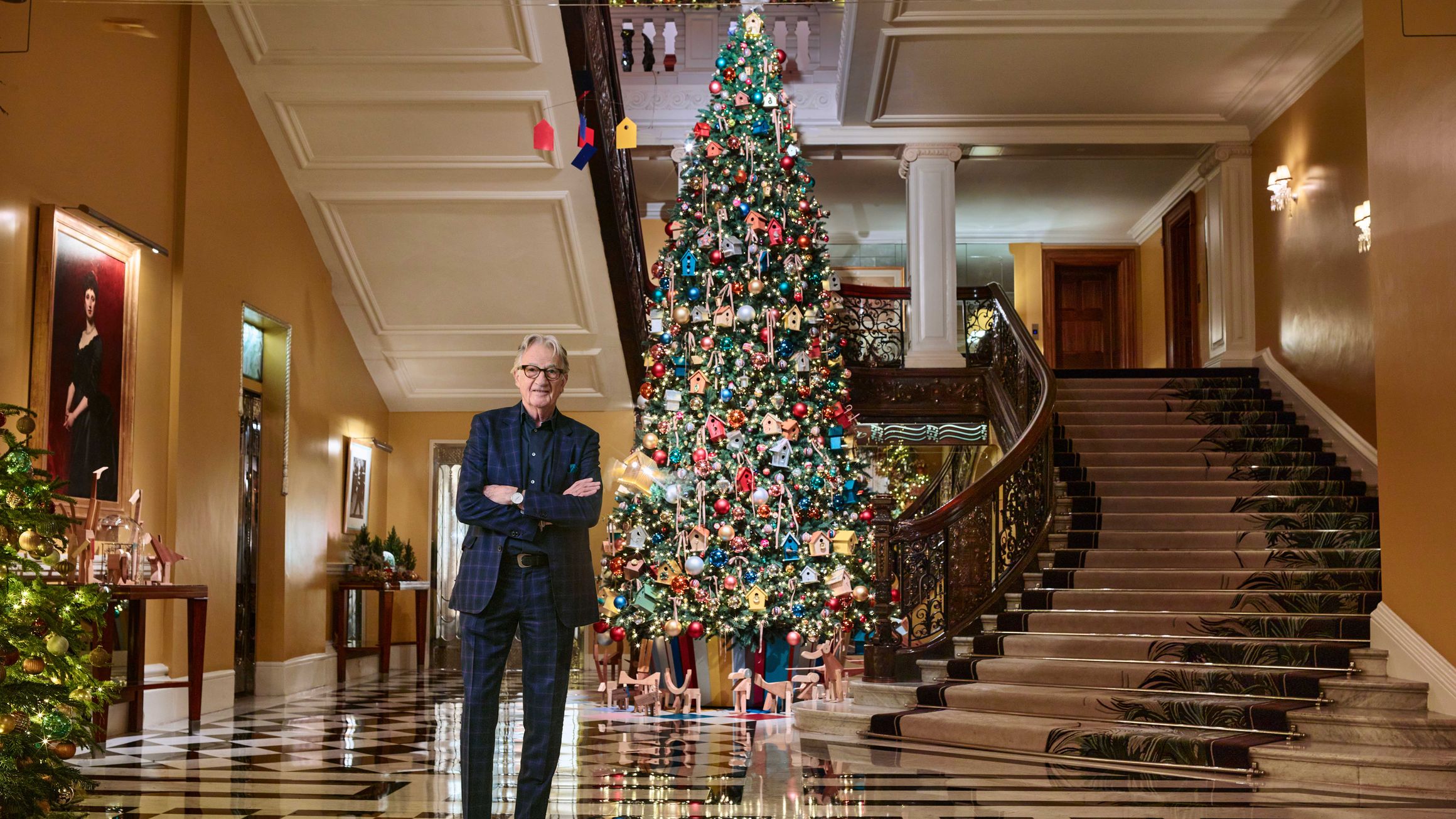 Sir Paul Smith stands beside the 2024 Claridge’s Christmas tree, decorated with colourful birdhouses and festive ornaments.