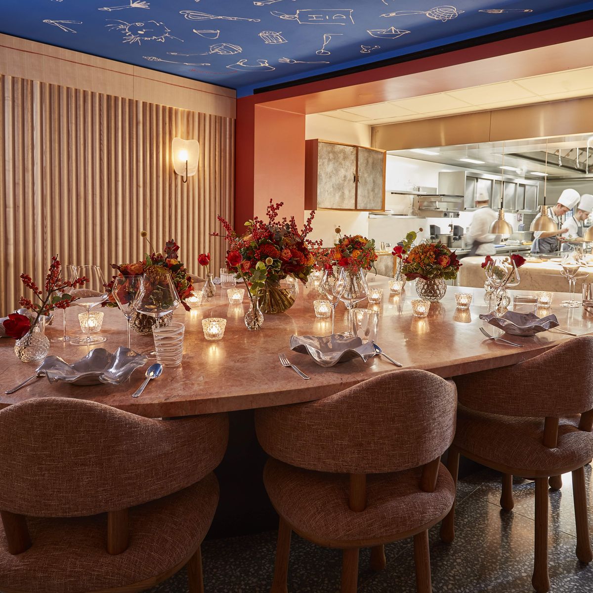 Chef's table experience with an intimate, beautifully decorated setting featuring floral arrangements, soft lighting, and a view into the kitchen.