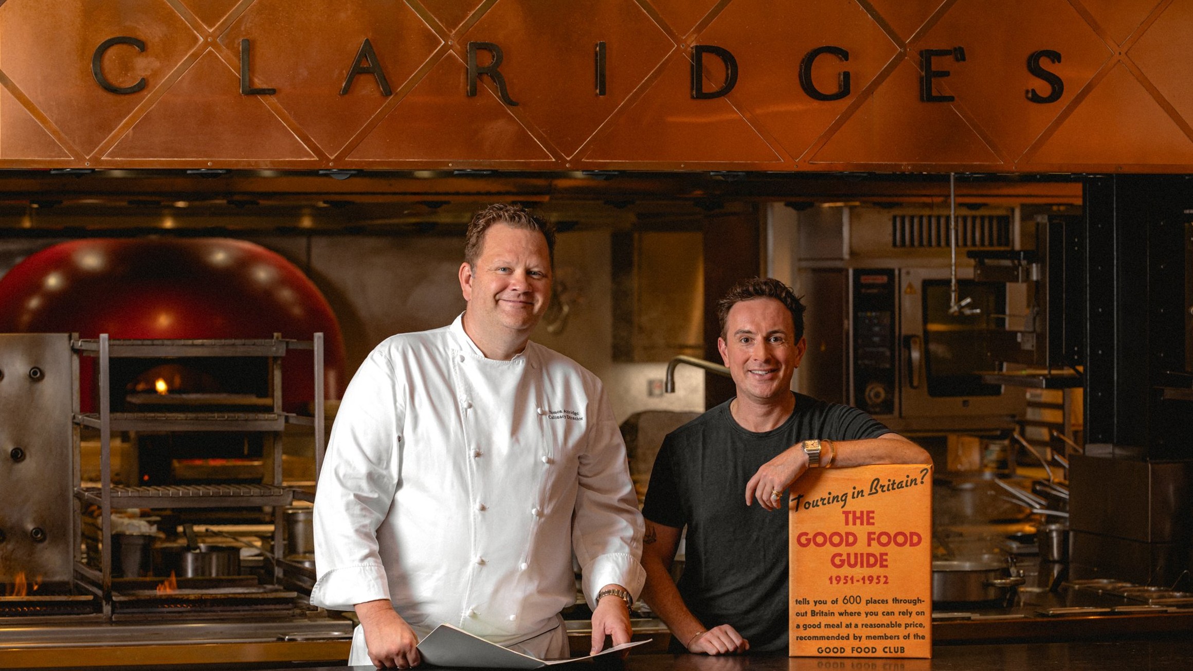 Claridge's chef stands confidently in a warm, copper-accented kitchen, showcasing culinary expertise and a refined professional ambiance.