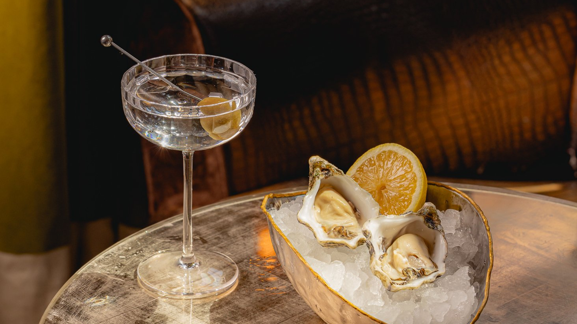Fresh oysters on ice with lemon, accompanied by a crystal-clear martini in an intimate, vintage-inspired lounge.