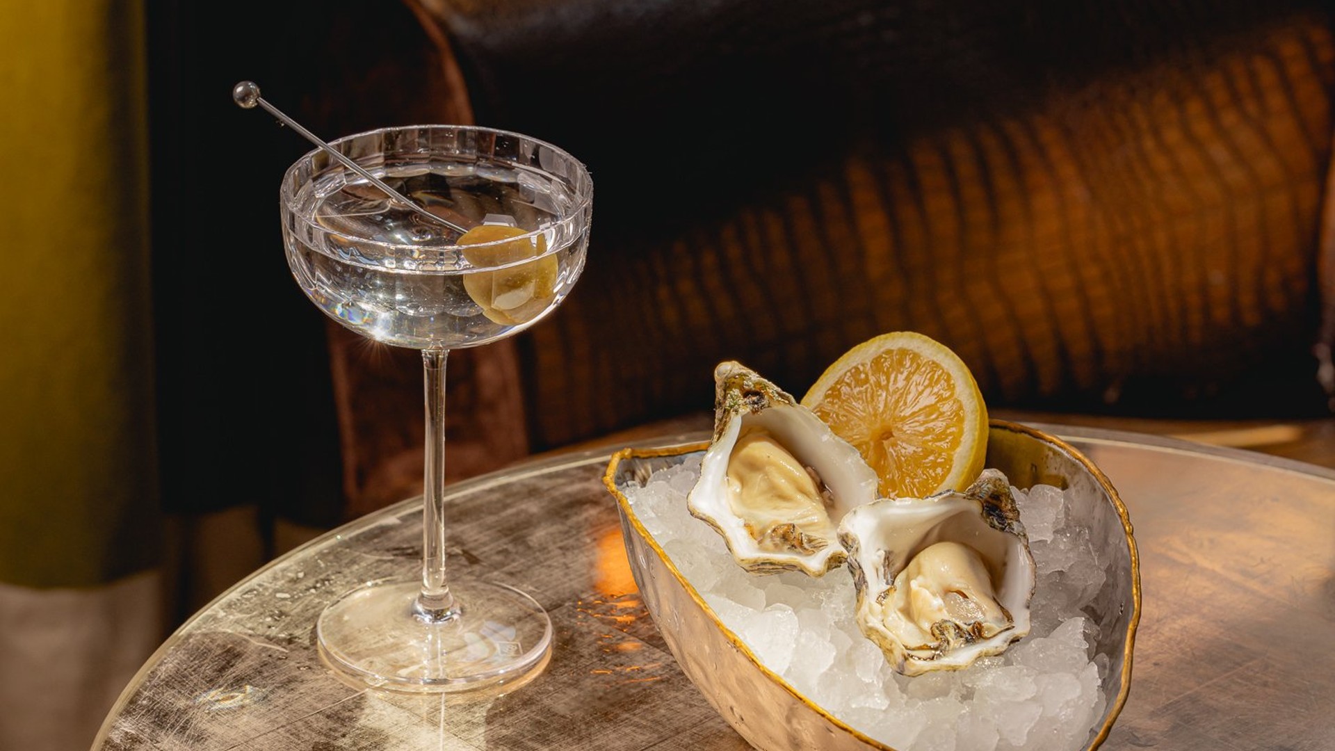 Fresh oysters on ice with lemon, accompanied by a crystal-clear martini in an intimate, vintage-inspired lounge.