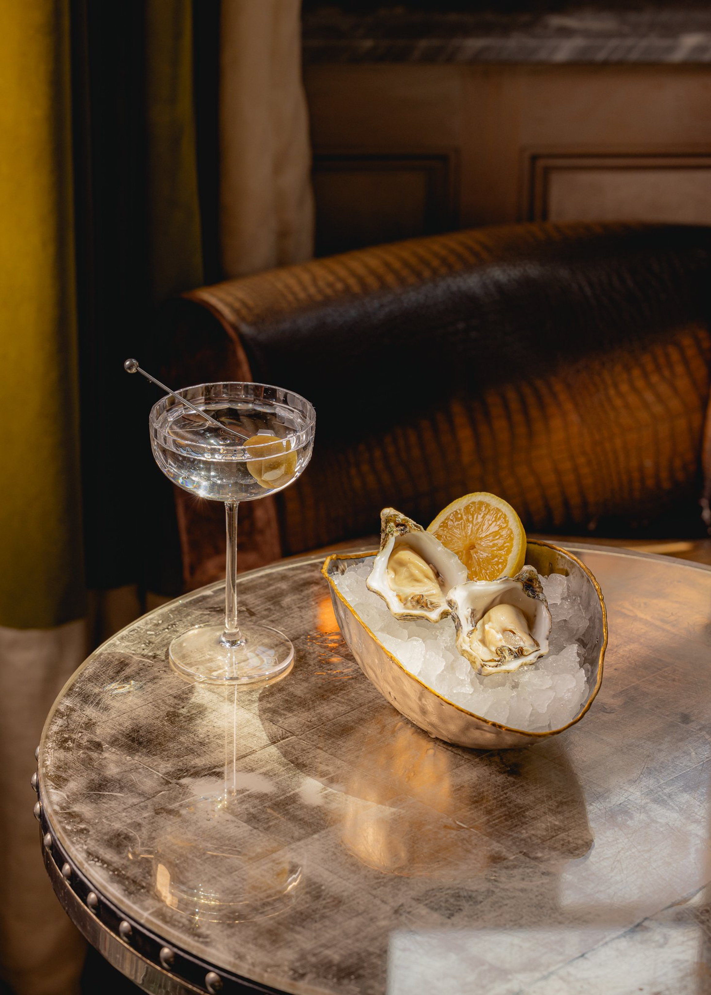 Fresh oysters on ice with lemon, accompanied by a crystal-clear martini in an intimate, vintage-inspired lounge.