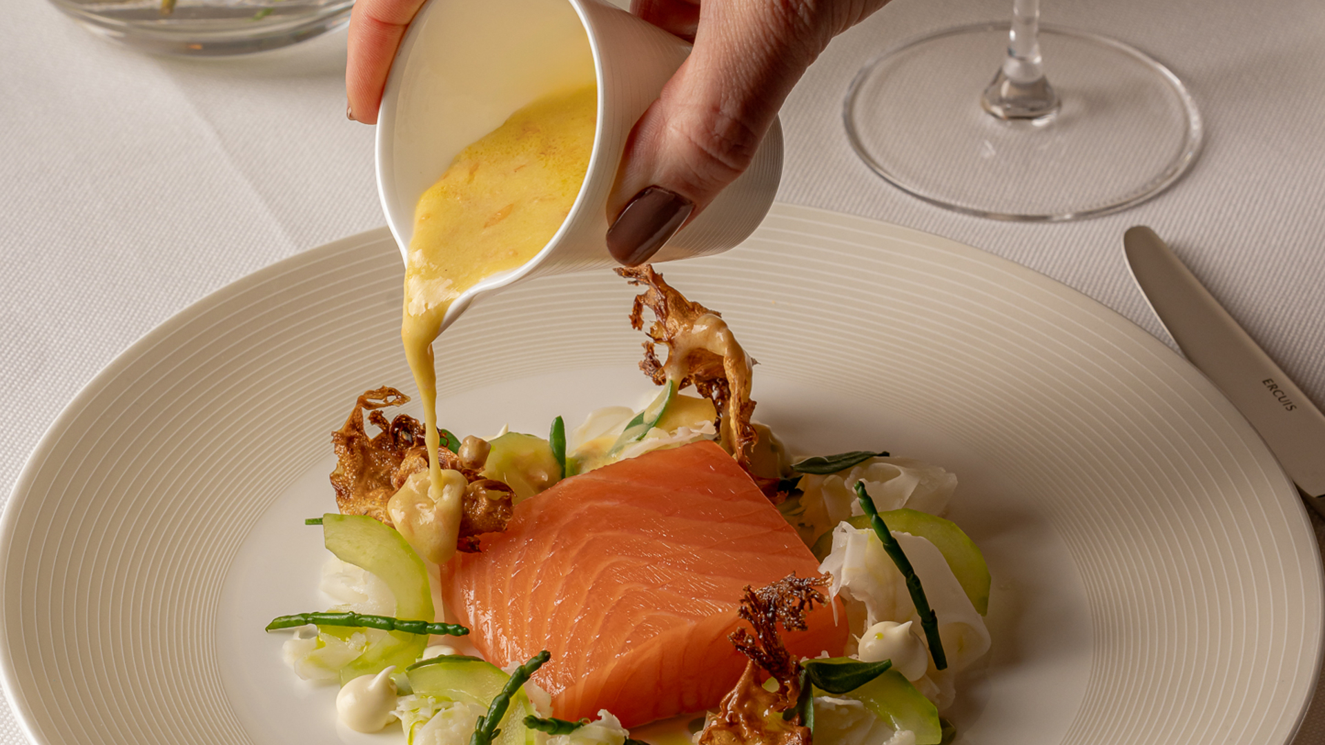 Delicately plated salmon with crisp accompaniments and rich sauce, presented with finesse in a sophisticated dining setting.
