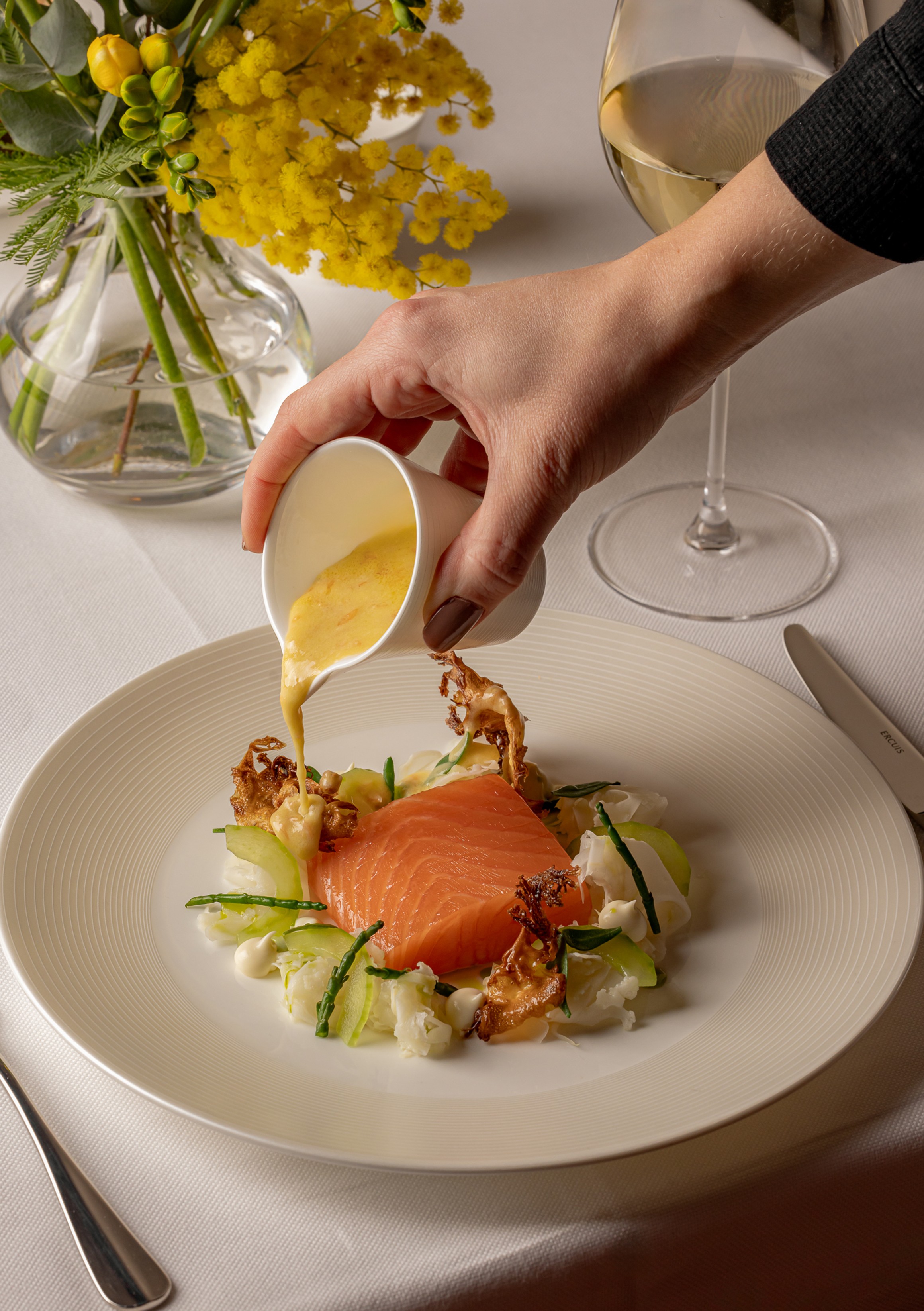 Delicately plated salmon with crisp accompaniments and rich sauce, presented with finesse in a sophisticated dining setting.