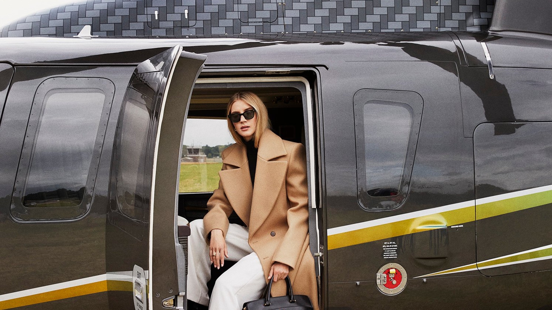 A stylish woman steps off a luxury helicopter onto The Emory London-branded mat, exuding sophistication and exclusivity.