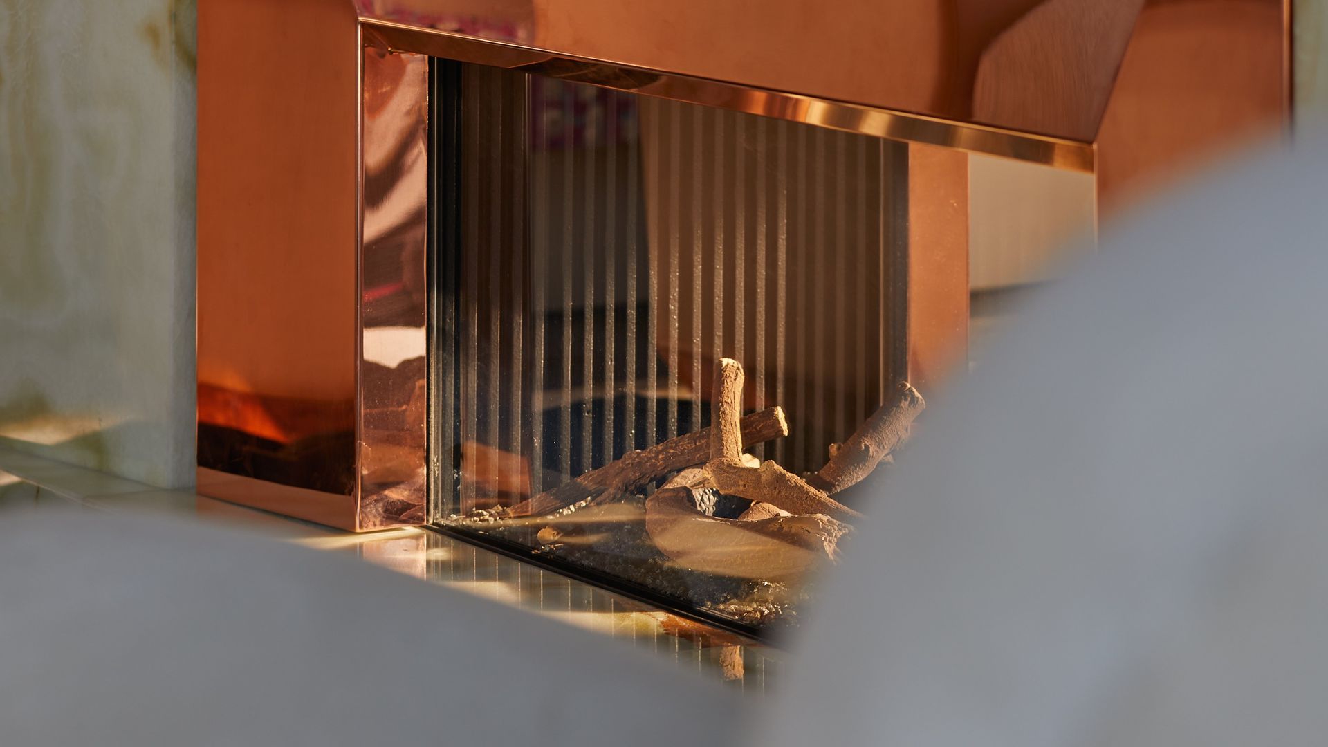 A polished copper-framed fireplace reflecting warm tones of surrounding furniture, juxtaposed against onyx-like stone.