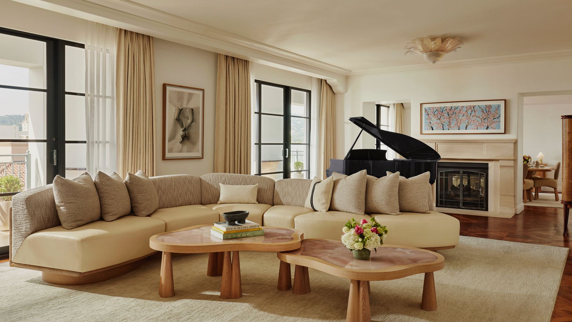 Spacious suite living room with curved sofa, baby grand piano, abstract artwork, and French doors to terrace.