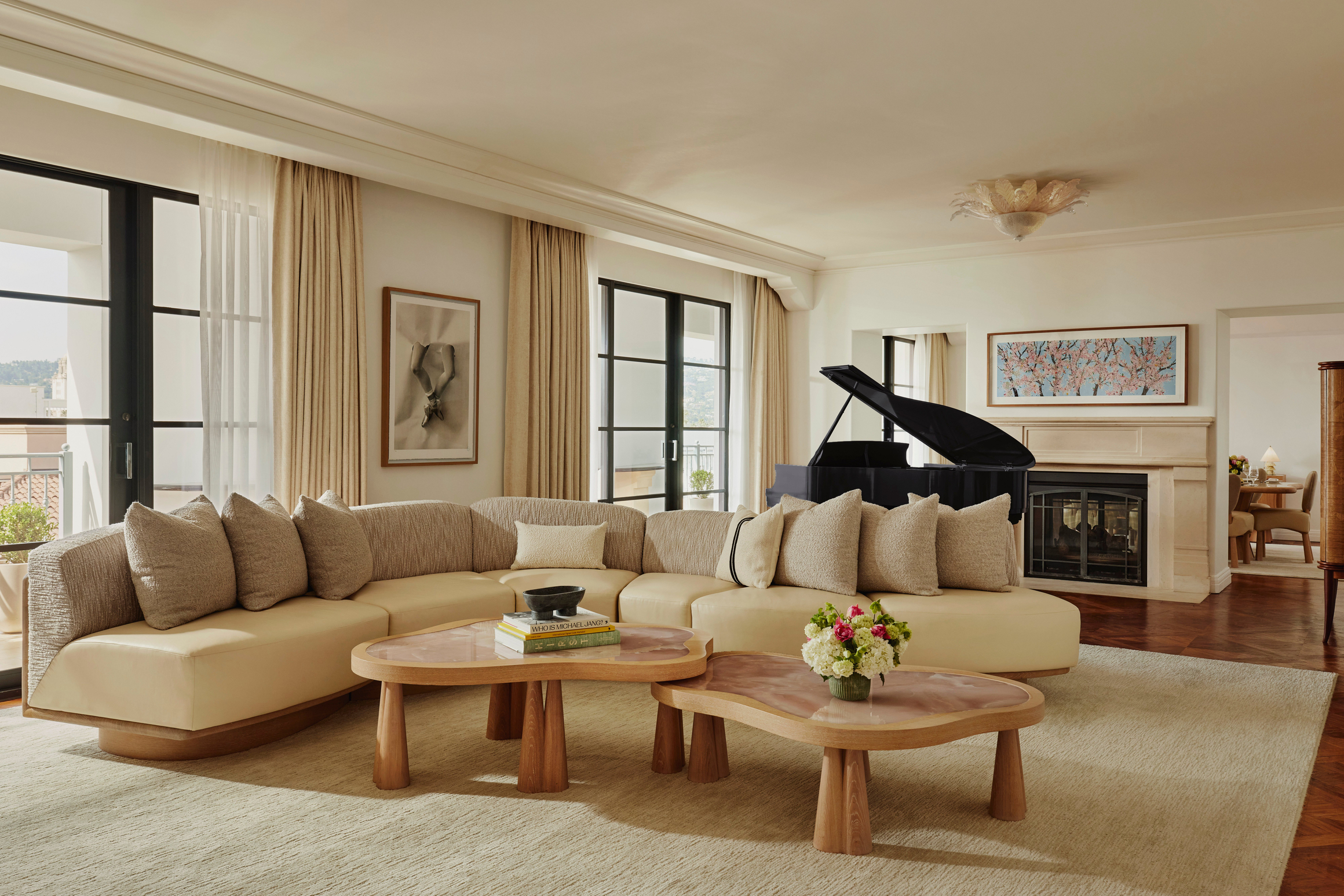 Spacious suite living room with curved sofa, baby grand piano, abstract artwork, and French doors to terrace.