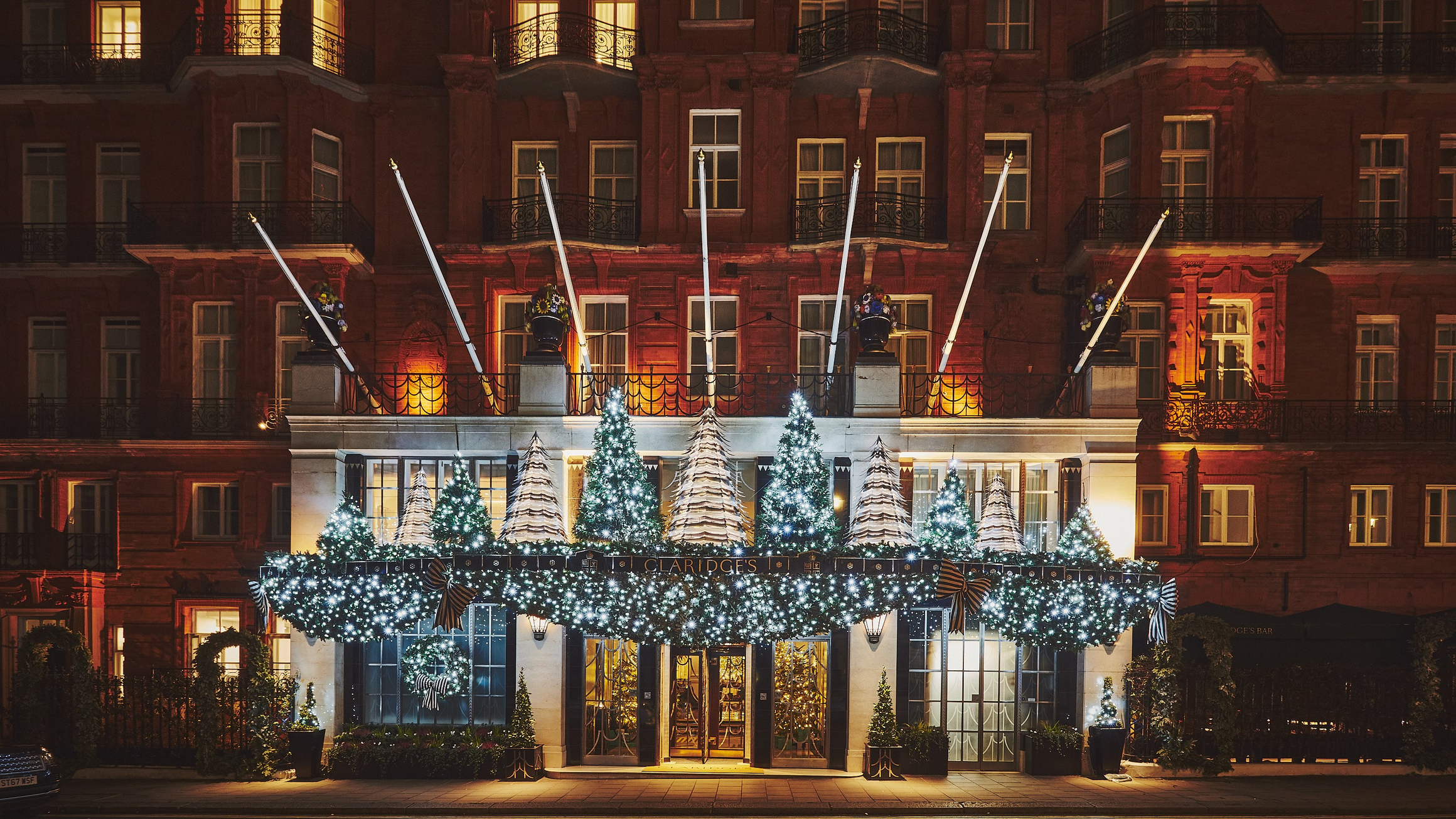 Close-up of Claridge’s entrance with illuminated Christmas garlands, large striped bows and evergreen trees