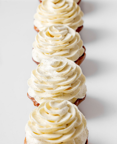 Row of small pastries topped with swirls of vanilla bean cream, arranged in a neat line on a white background.