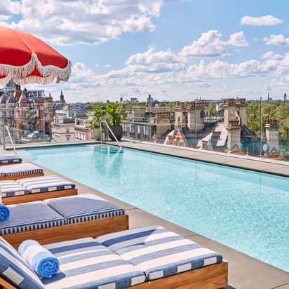 Rooftop pool with striped loungers, red parasols, and skyline views over London and Hyde Park.