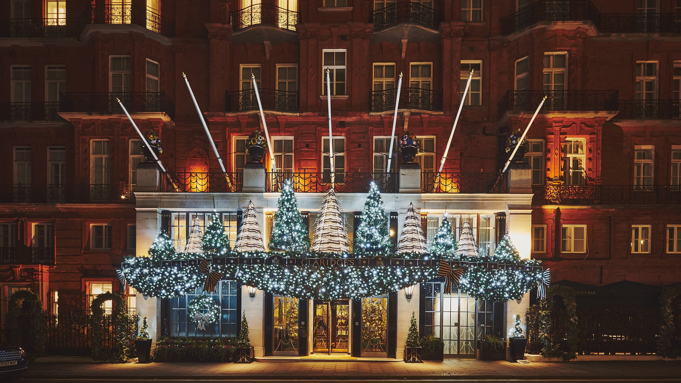 Claridge’s exterior decorated with lit Christmas trees, garlands and warm window lights at night