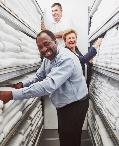 Three smiling staff members stand between shelves stacked with neatly folded white towels embroidered with "The Berkeley" logo.