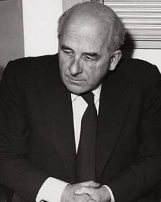 Black-and-white portrait of a thoughtful man in a suit, hands folded, exuding a sense of introspective elegance