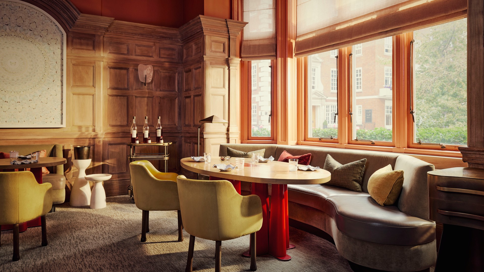 Intimate dining room with curved banquette, wood-paneled walls, and tall sash windows overlooking a classic London street..