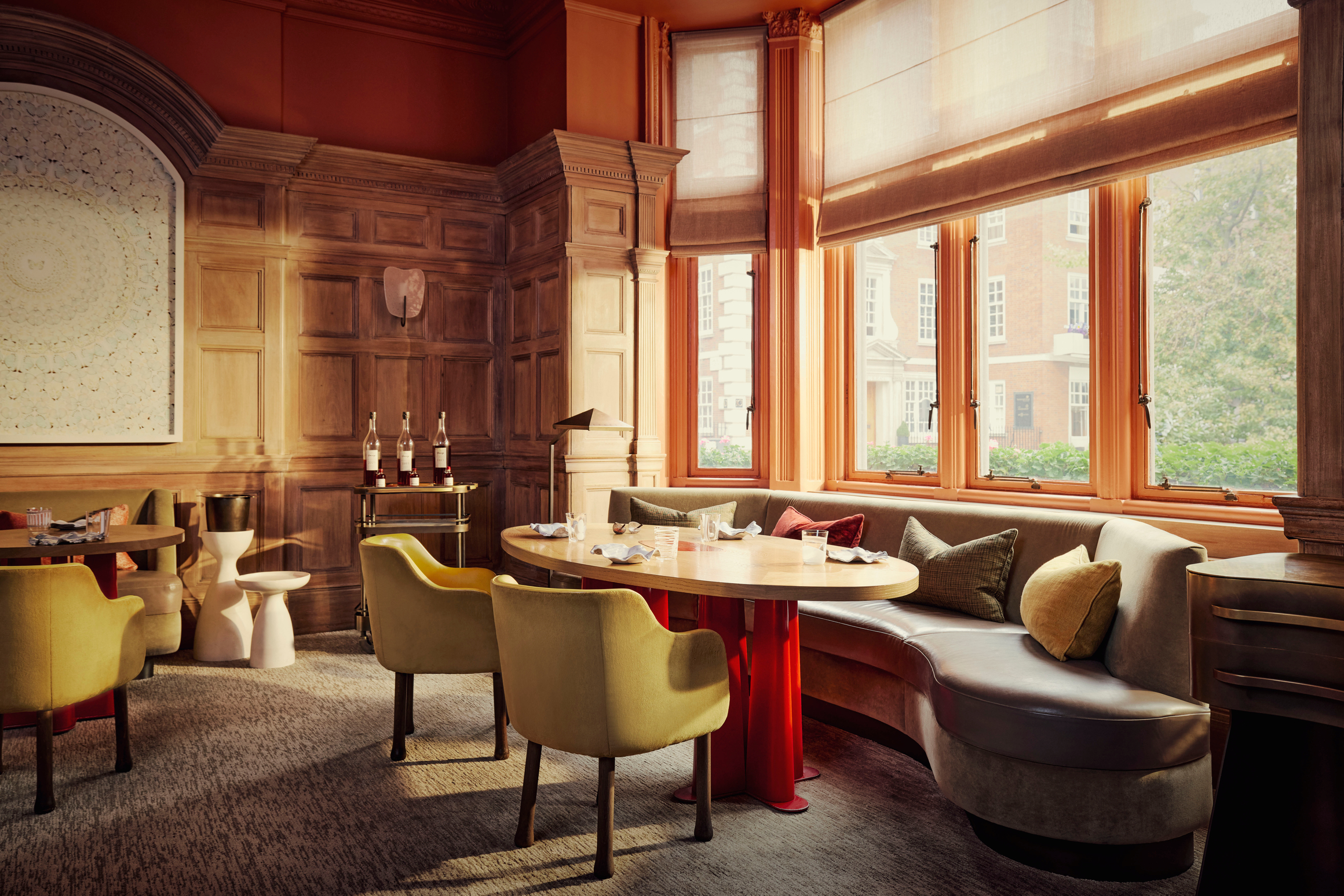 Intimate dining room with curved banquette, wood-paneled walls, and tall sash windows overlooking a classic London street..