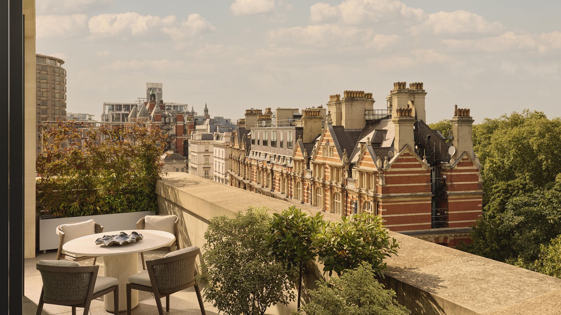Rooftop terrace with dining table overlooking historic red-brick buildings in London.