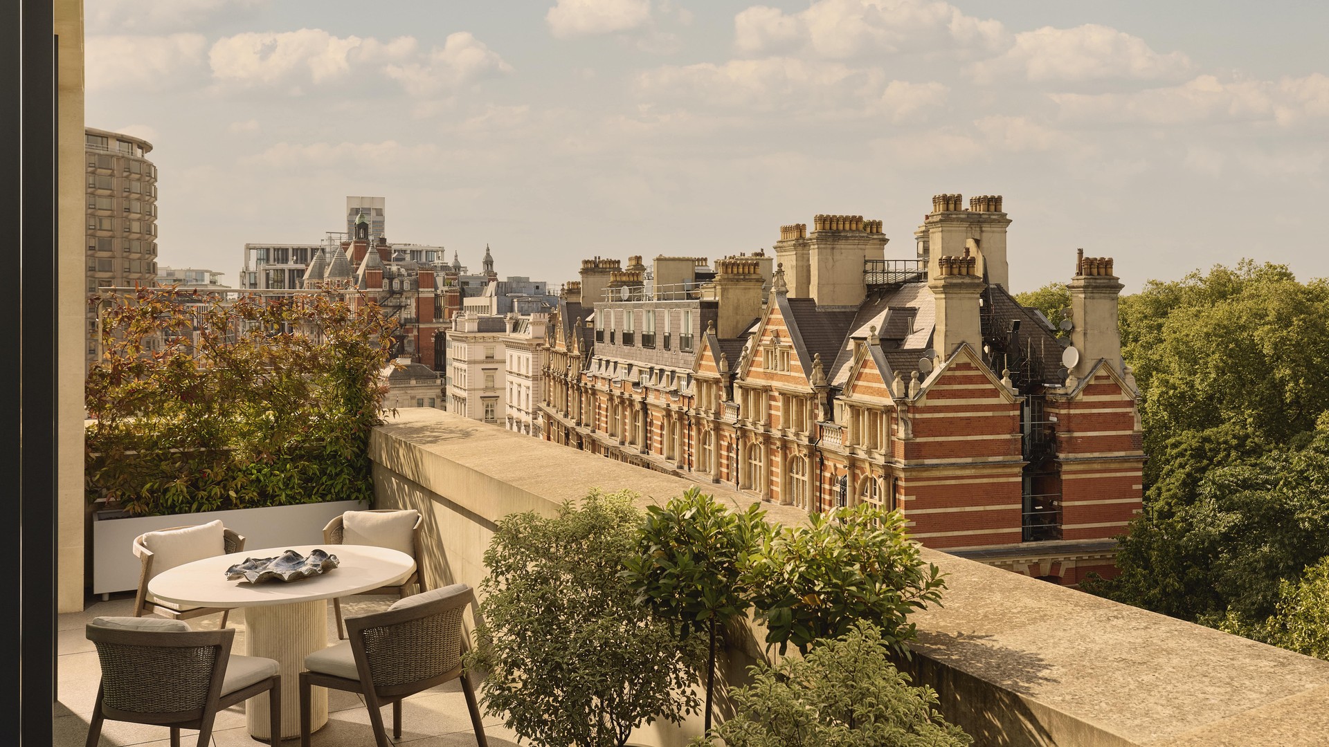 Rooftop terrace with dining table overlooking historic red-brick buildings in London.