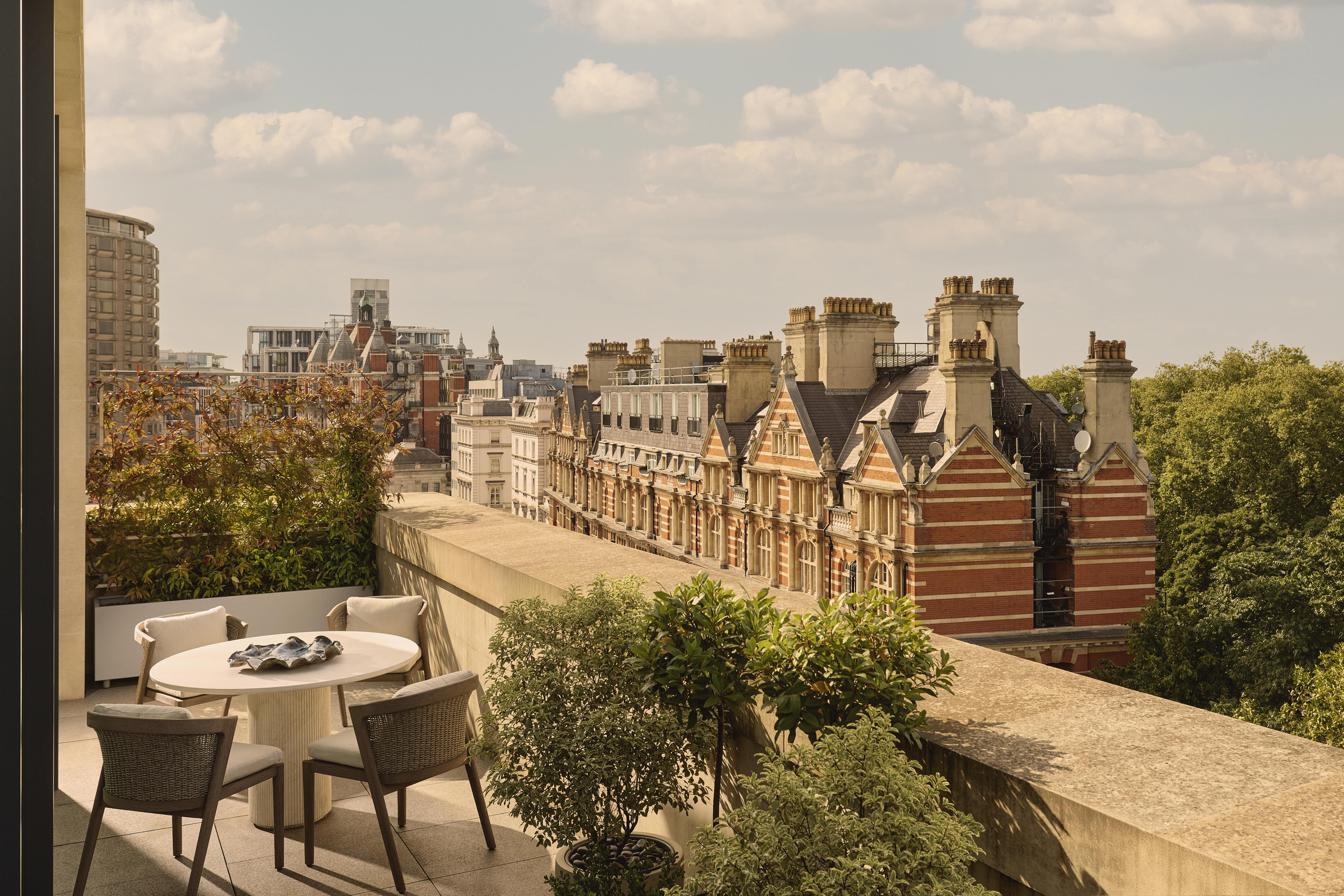 Rooftop terrace with dining table overlooking historic red-brick buildings in London.