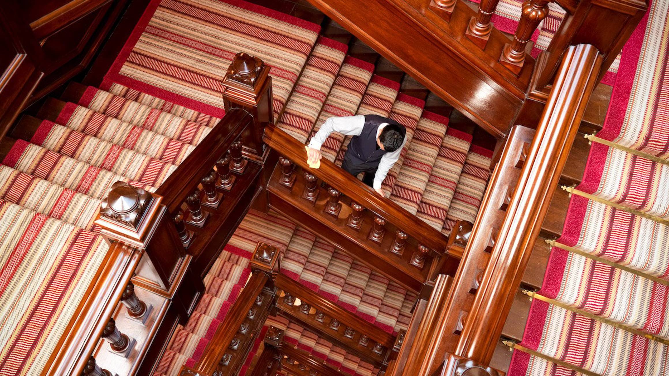 Spiraling polished wood staircase with striped carpeting, epitomizing opulence and impeccable craftsmanship.