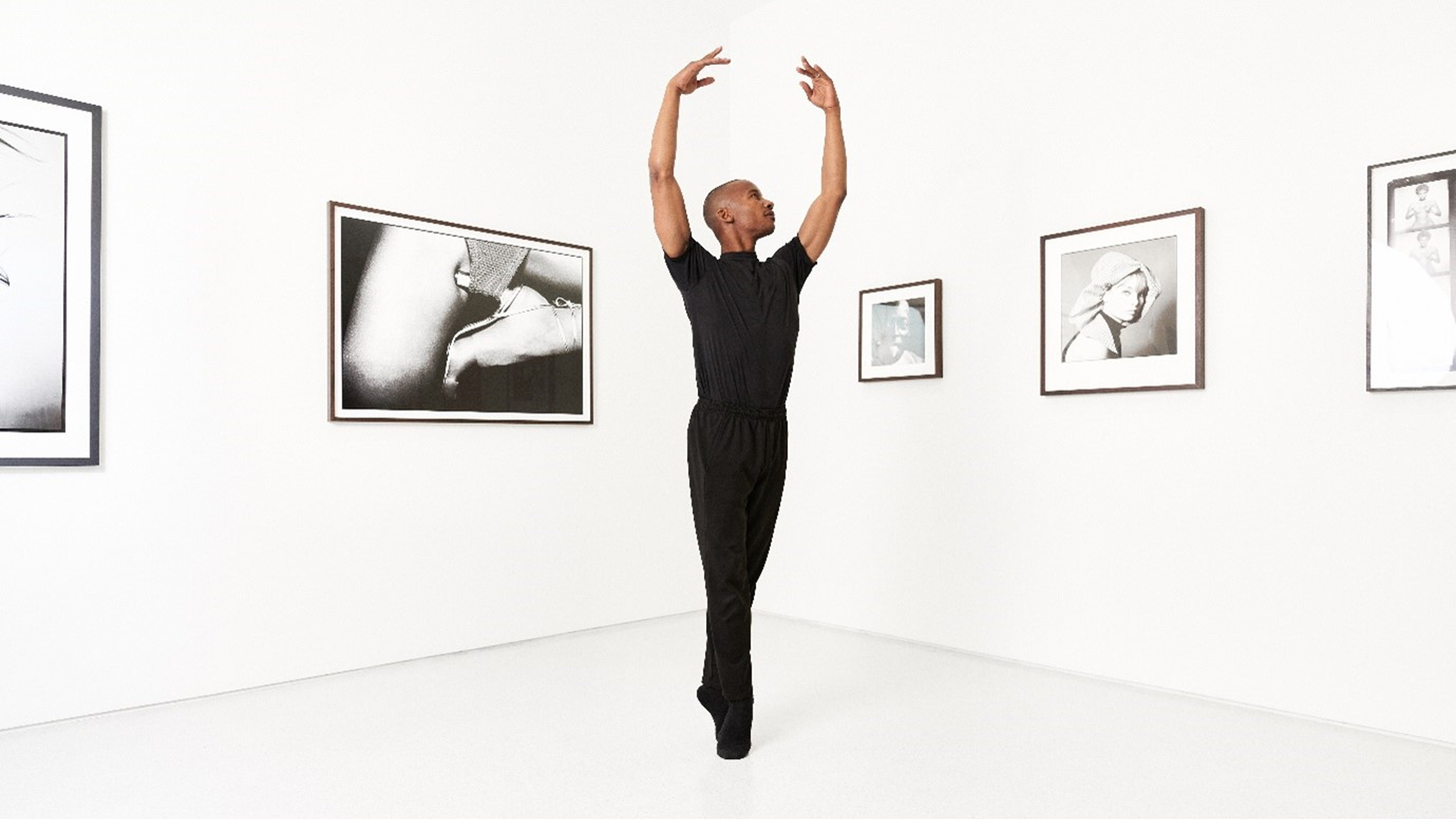 A dancer gracefully poses in a minimalist gallery space, surrounded by monochrome photography, embodying elegance and artistic expression.